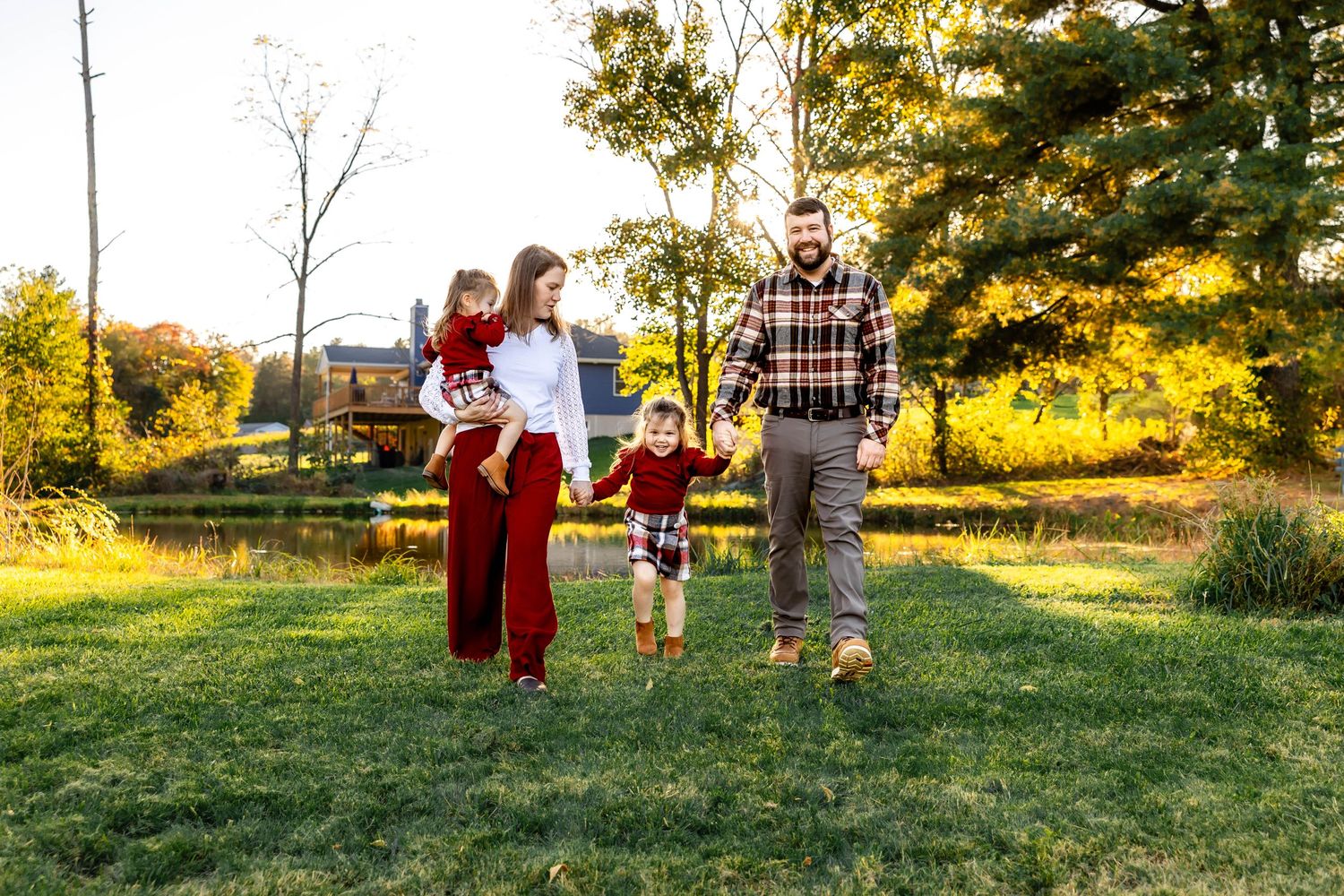 Family holding hands while walking through sunlit field during autumn photoshoot.