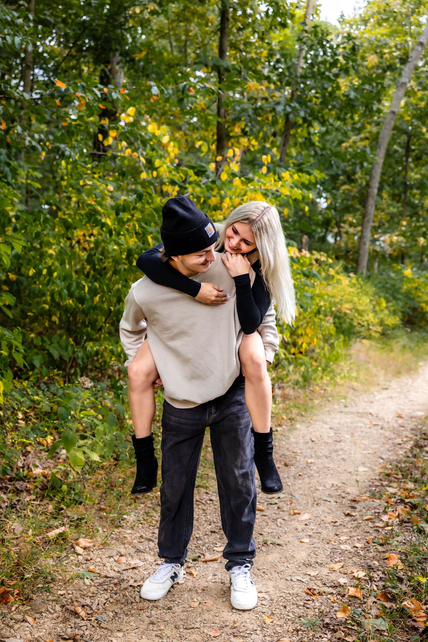 A couple embraces on a nature trail surrounded by autumn foliage.