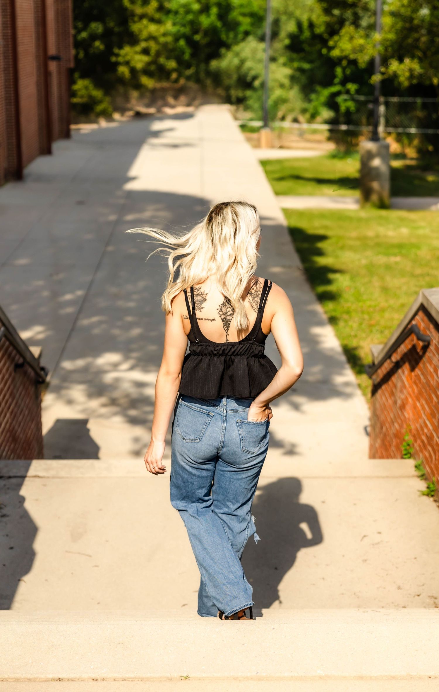 Back view walking shot showing black top and blue jeans along brick walkway.