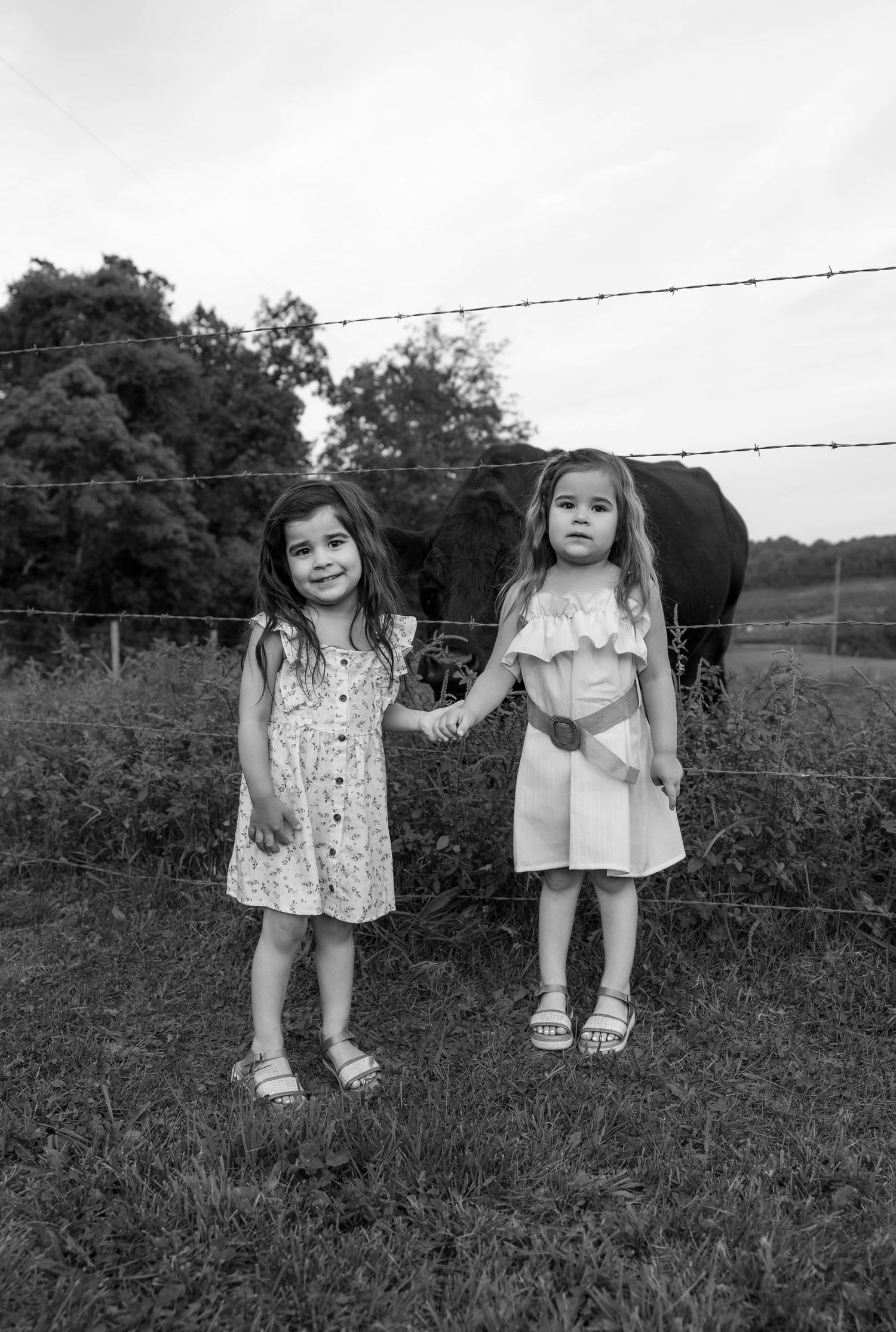 Black and white countryside portrait of two children standing by a barbed wire fence.