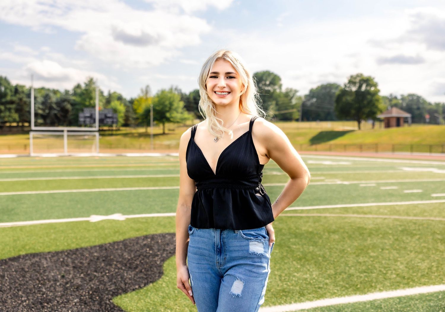 Casual outdoor portrait on football field with black top and distressed jeans.