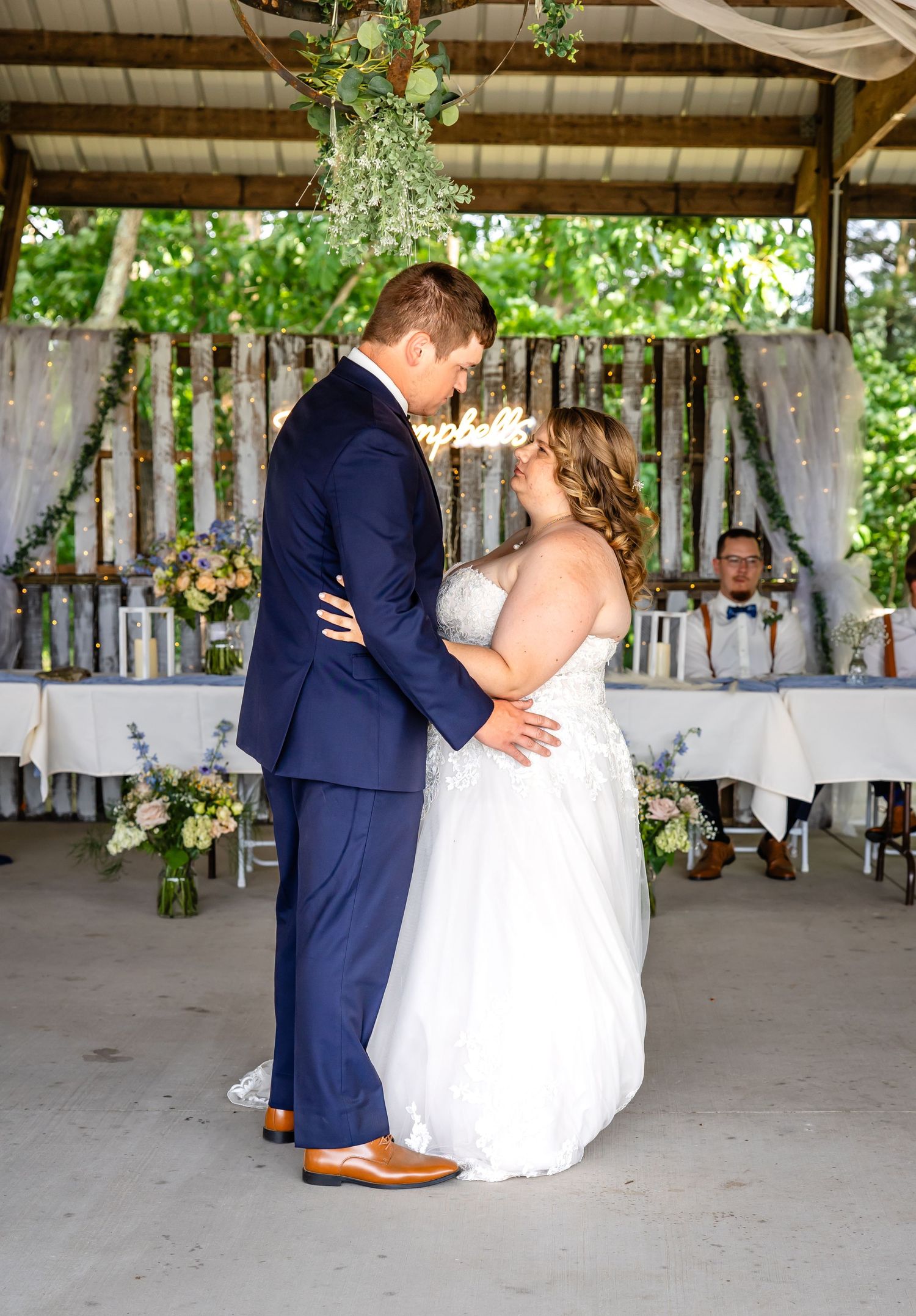 A newlywed couple embraces during their wedding reception under a decorated pavilion.