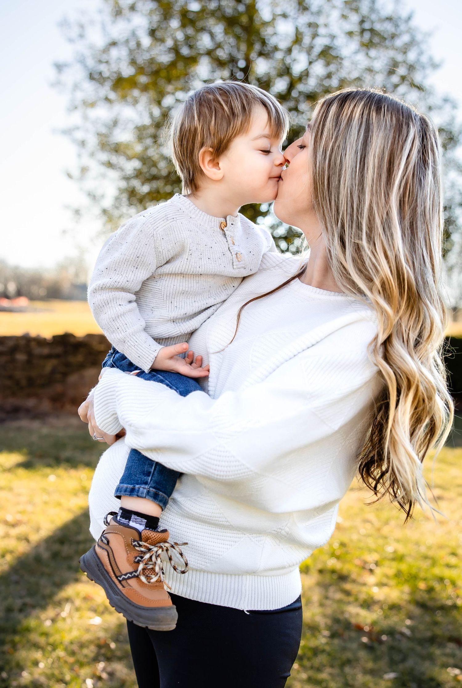 Sweet moment between parent and child outdoors wearing matching white sweaters.