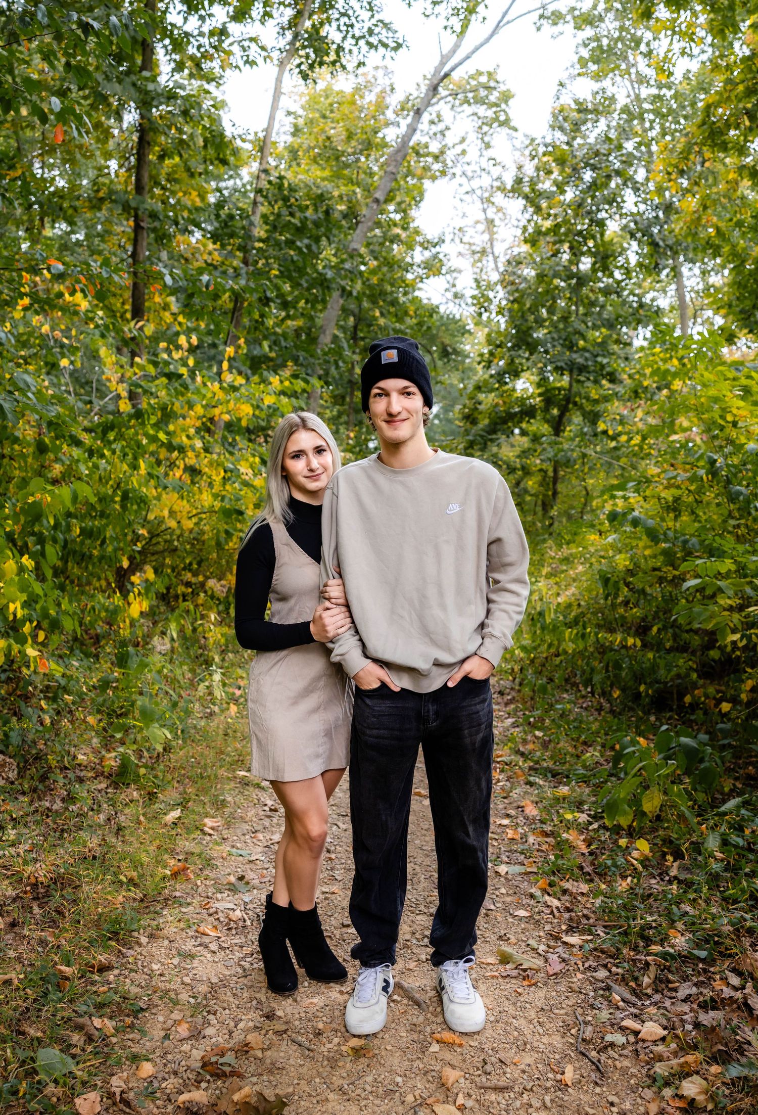 Couple standing on autumn forest path surrounded by yellow and green leaves.