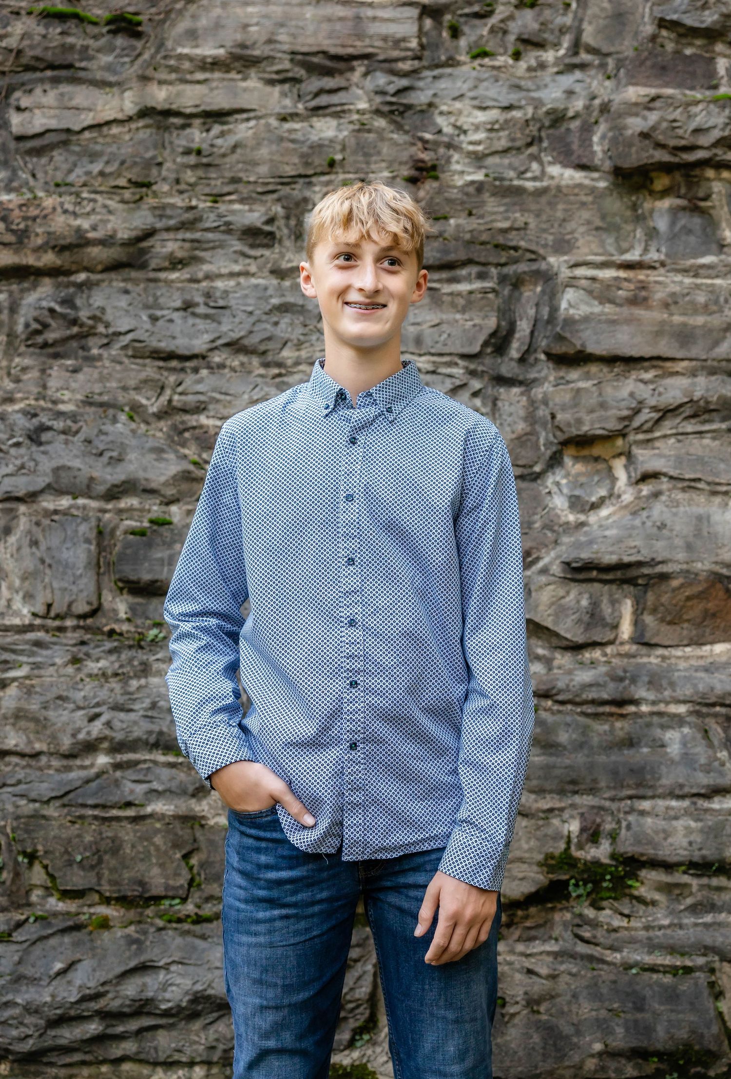 A casual portrait against a stone wall backdrop in natural lighting.
