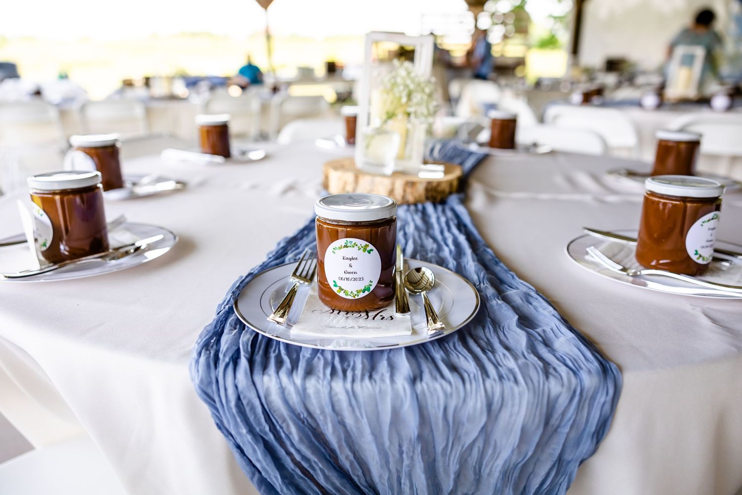 Wedding reception table setting with blue runner and mason jar favors.
