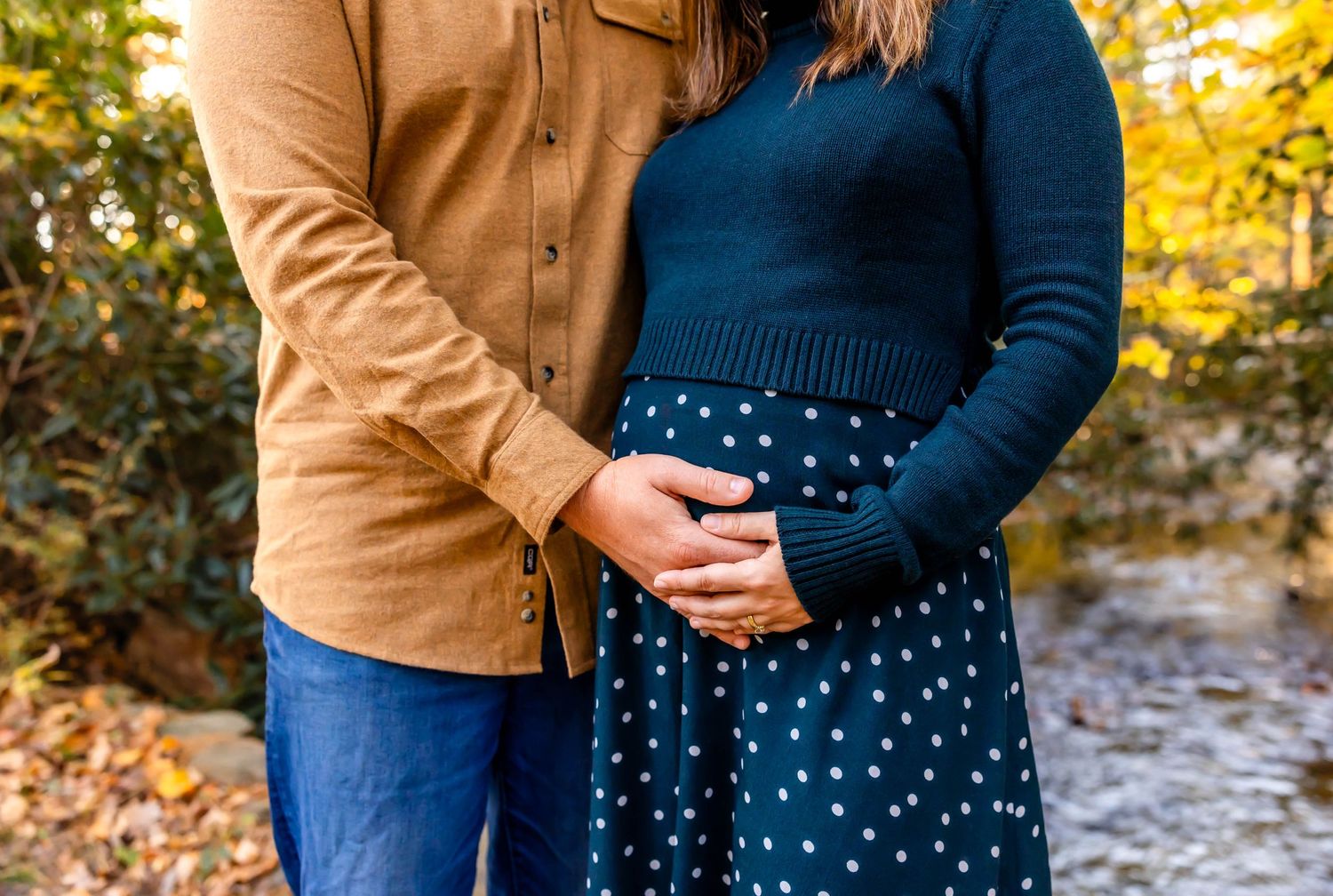 Close-up of couple's hands resting on maternity dress with polka dot pattern.