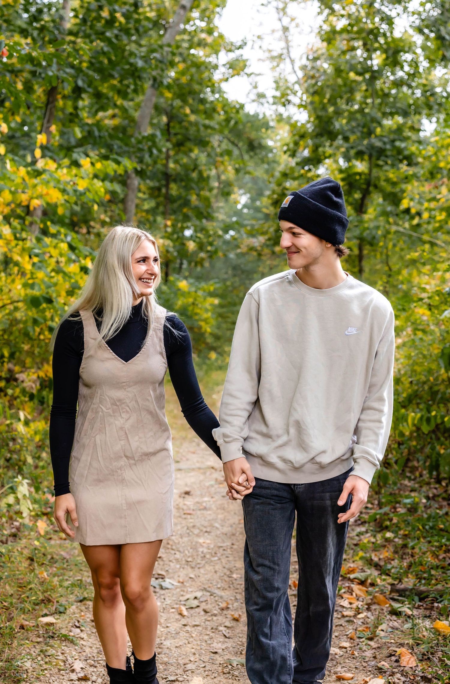 A couple shares a joyful moment while walking hand in hand on a wooded trail in autumn.