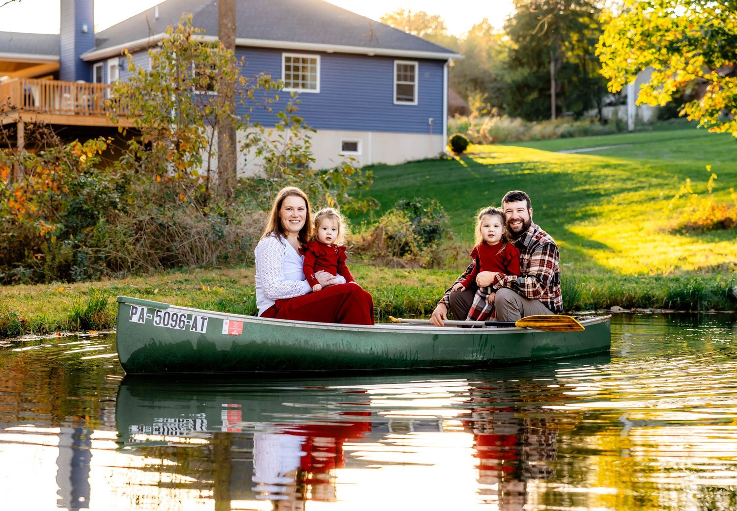 People enjoy a serene canoe ride by a blue house as autumn colors reflect on calm waters.