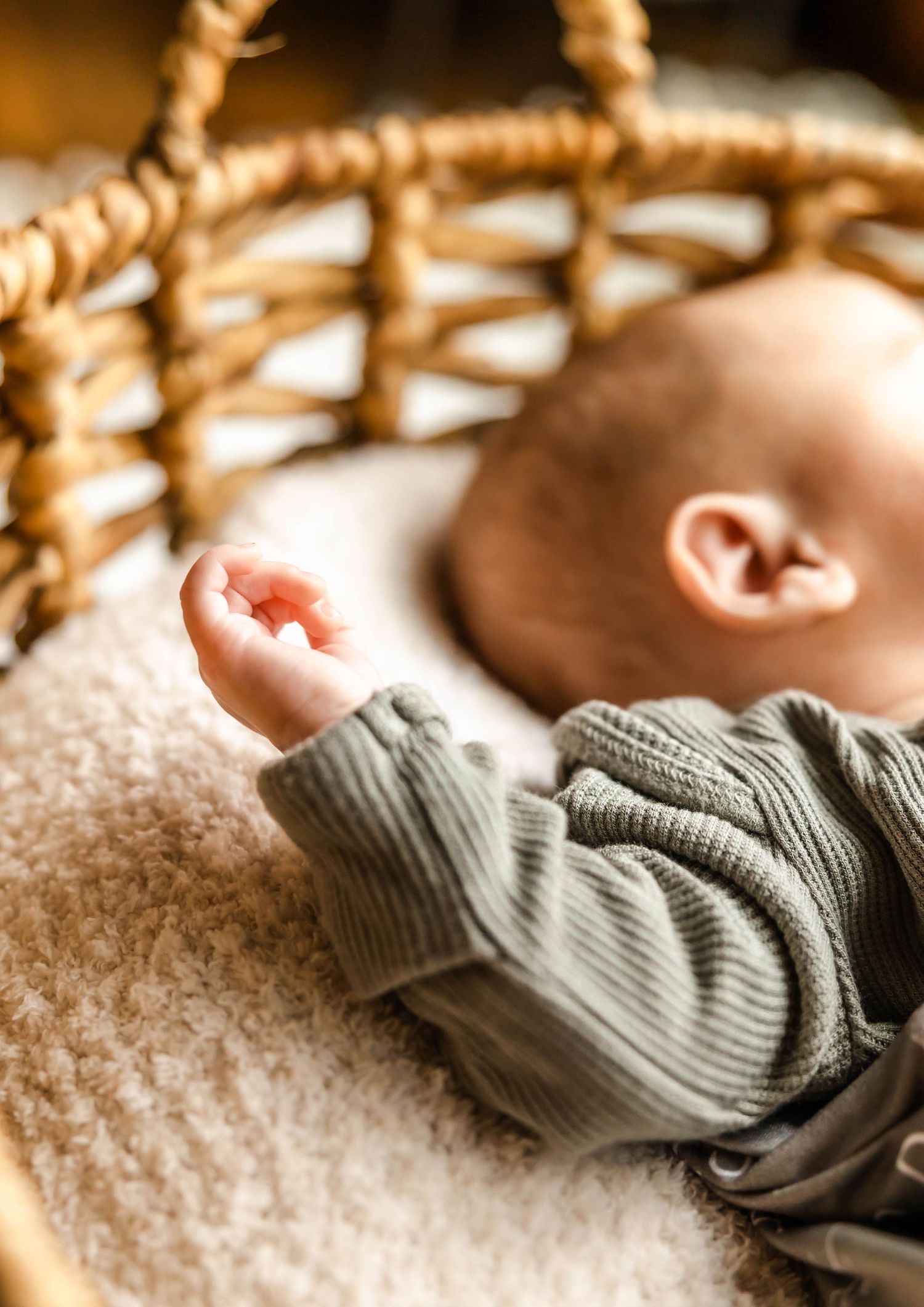 Close up of small baby hand reaching up from gray sweater in woven basket.