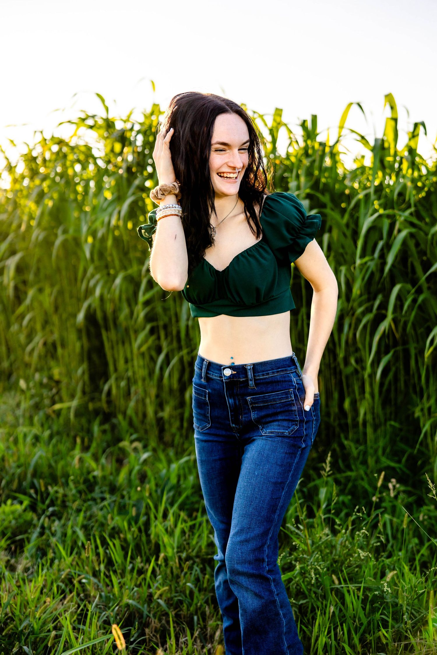 Summer fashion portrait with a dark crop top and jeans against tall green cornstalks.