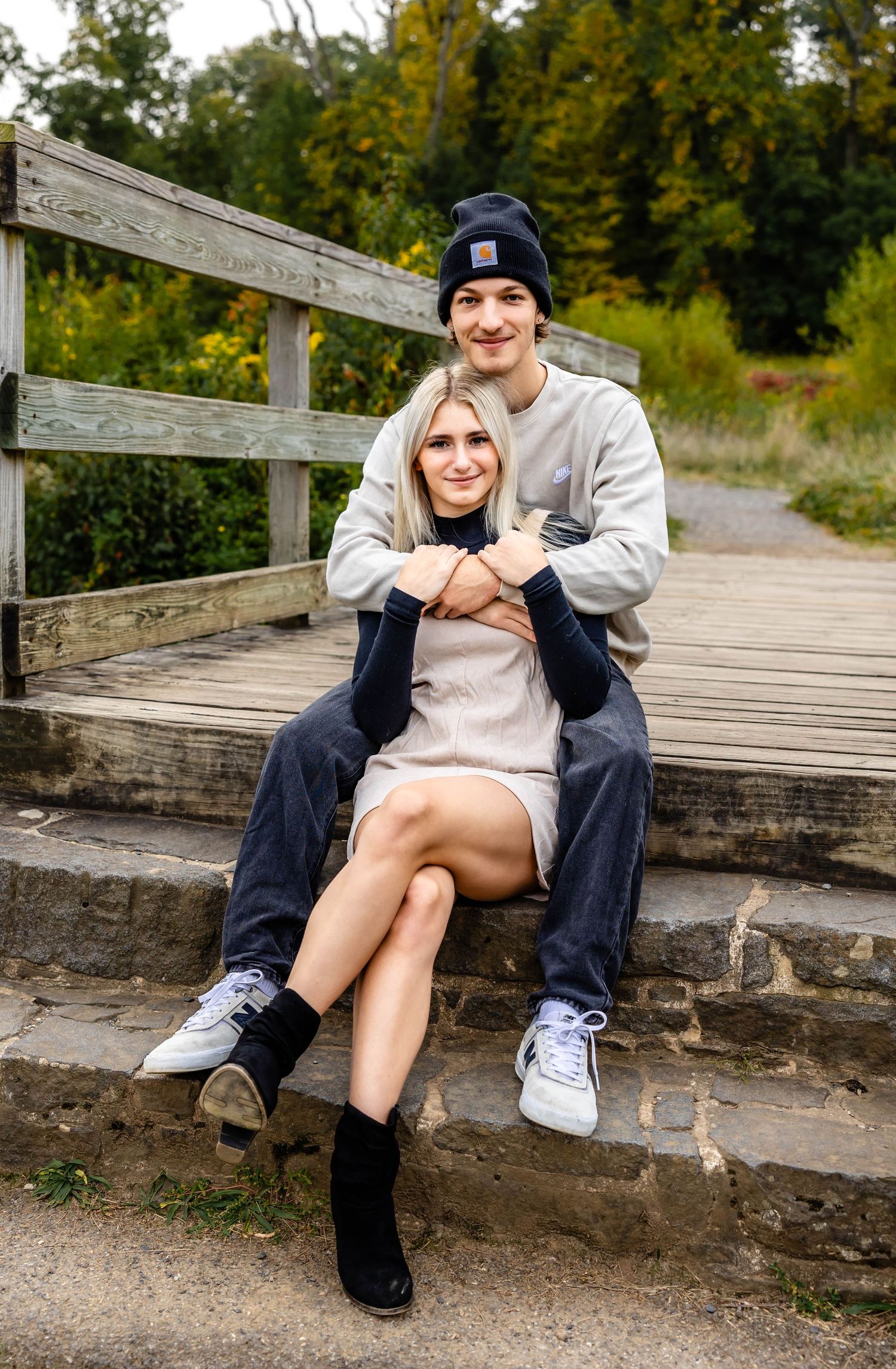 Cozy couple embraces on rustic wooden bridge steps during autumn photo session.