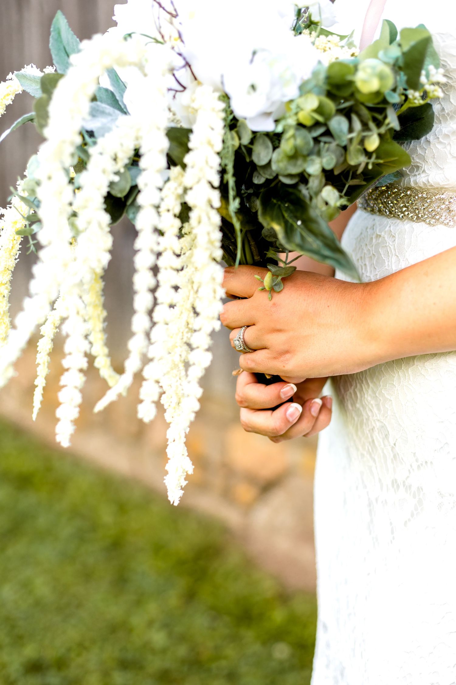 Bridal bouquet featuring dramatic white hanging amaranthus and mixed foliage against a white dress.