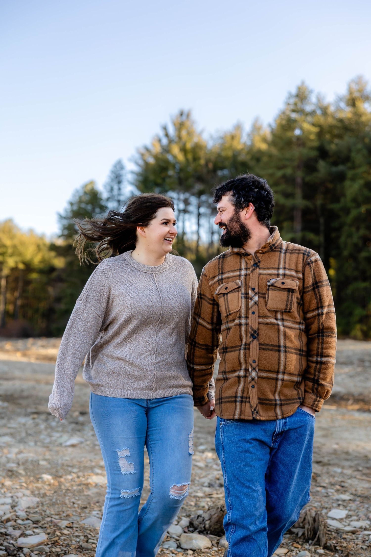 A couple walks together outdoors, wearing casual attire against a wooded background.