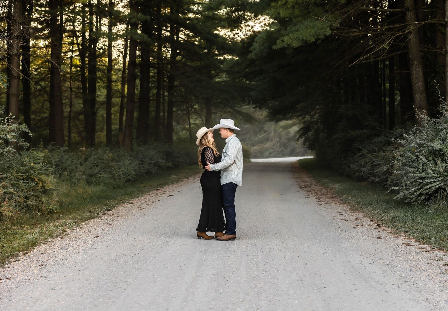 A romantic couple stands close together on a misty forest path at dusk.