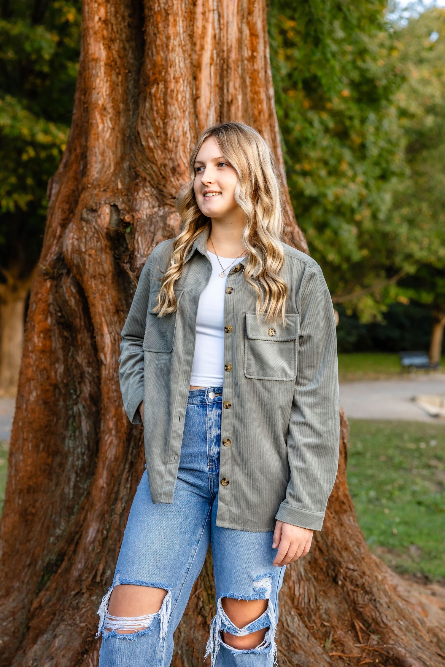 Autumn outdoor portrait with person wearing gray jacket and ripped jeans against textured tree bark.