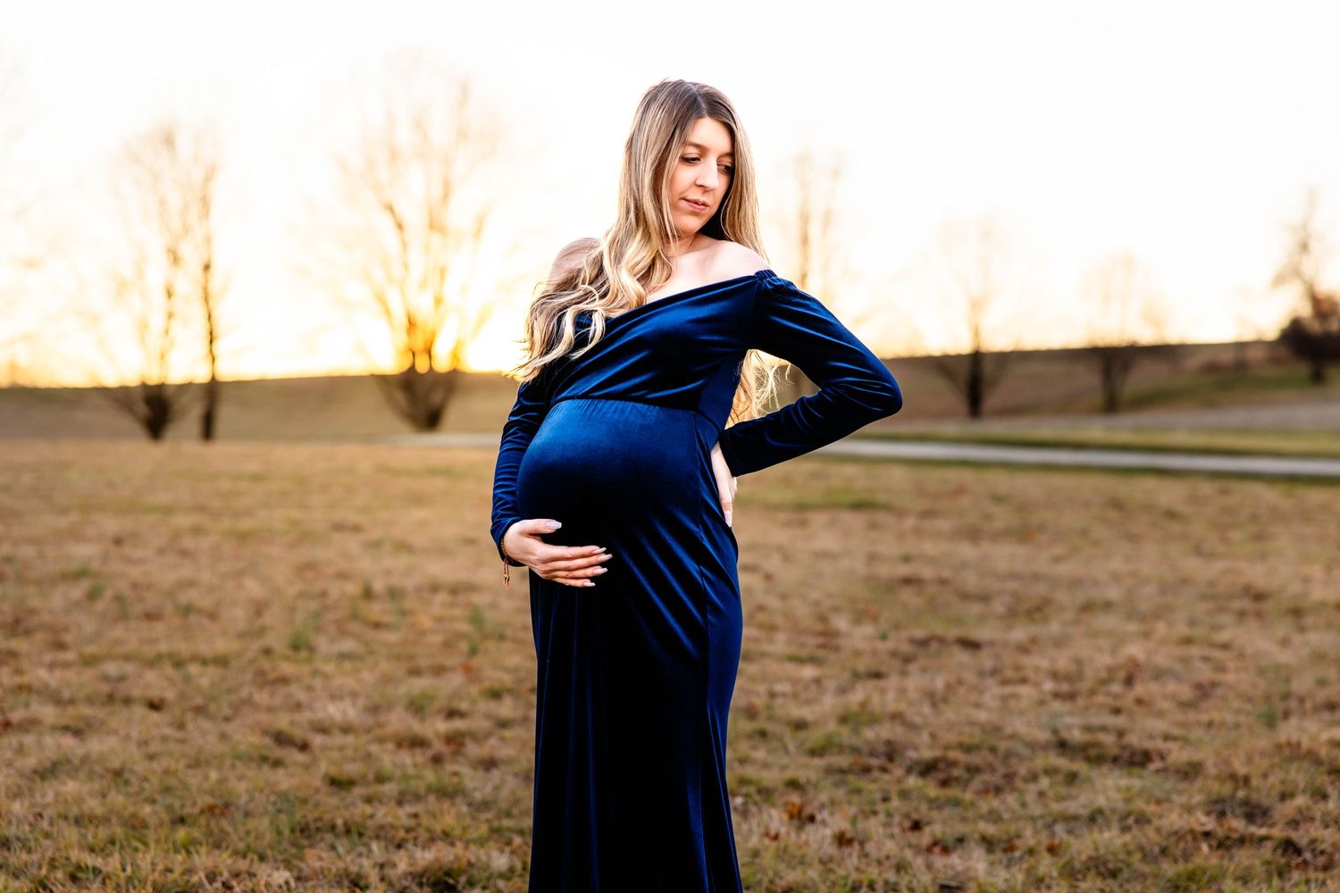 Side view maternity portrait in deep blue velvet gown during sunset.