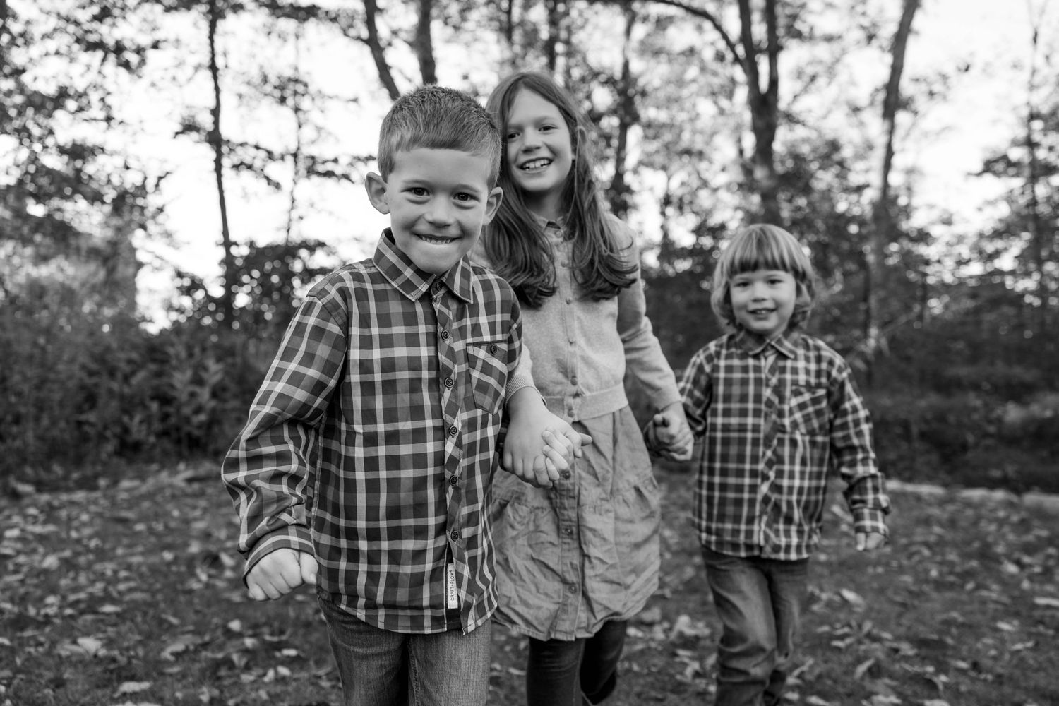 Children in plaid shirts play together among fallen autumn leaves.