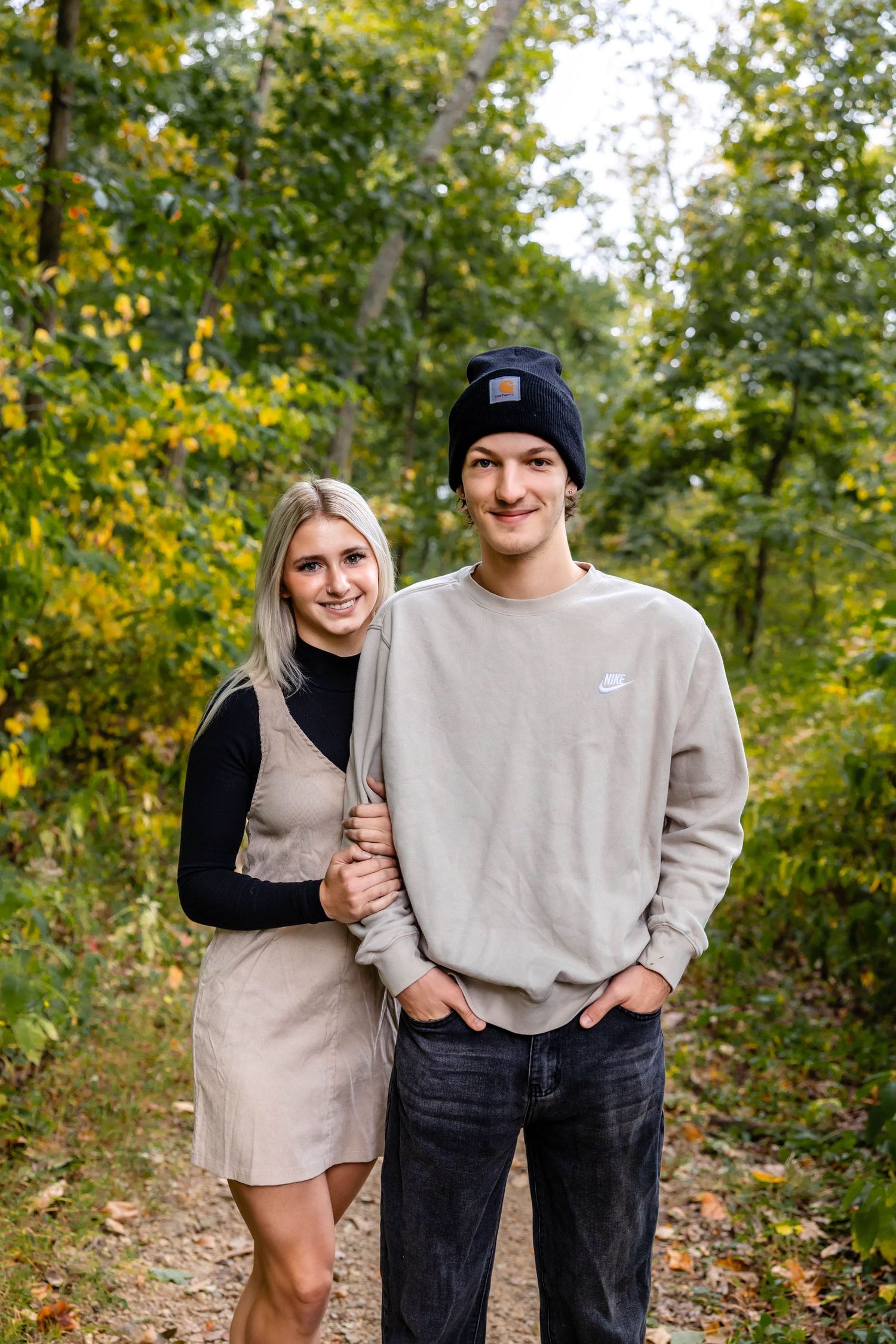 Young couple posing together on autumn trail surrounded by yellow and green foliage.