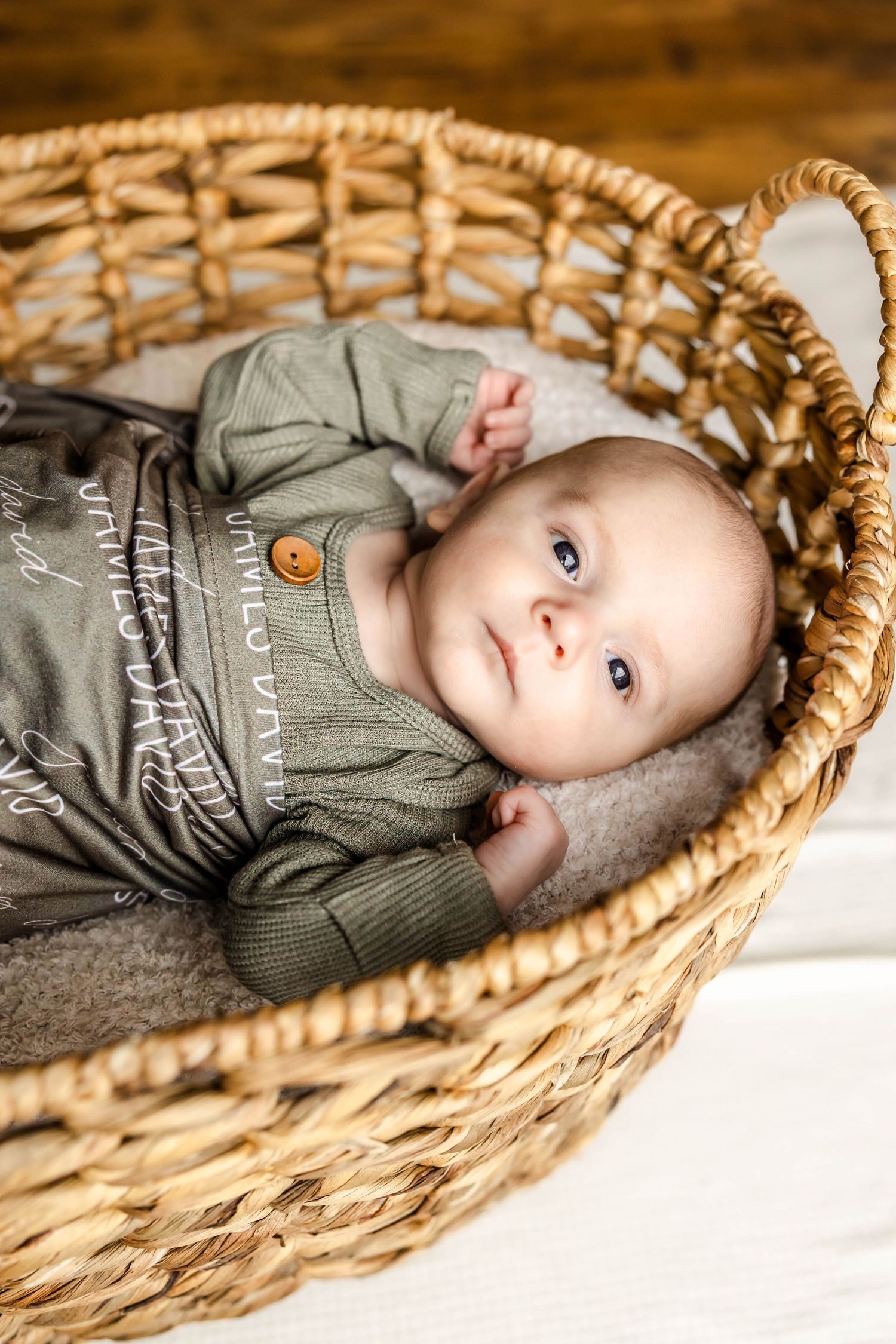 Baby in gray outfit resting inside rustic woven basket with cream colored lining.