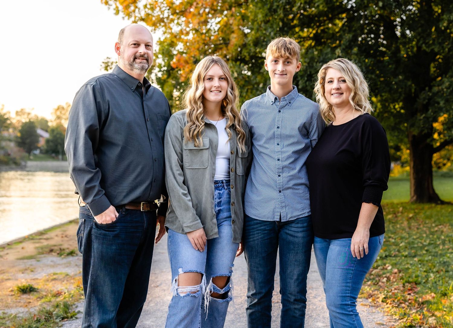 Family group poses together on path by river during autumn sunset.