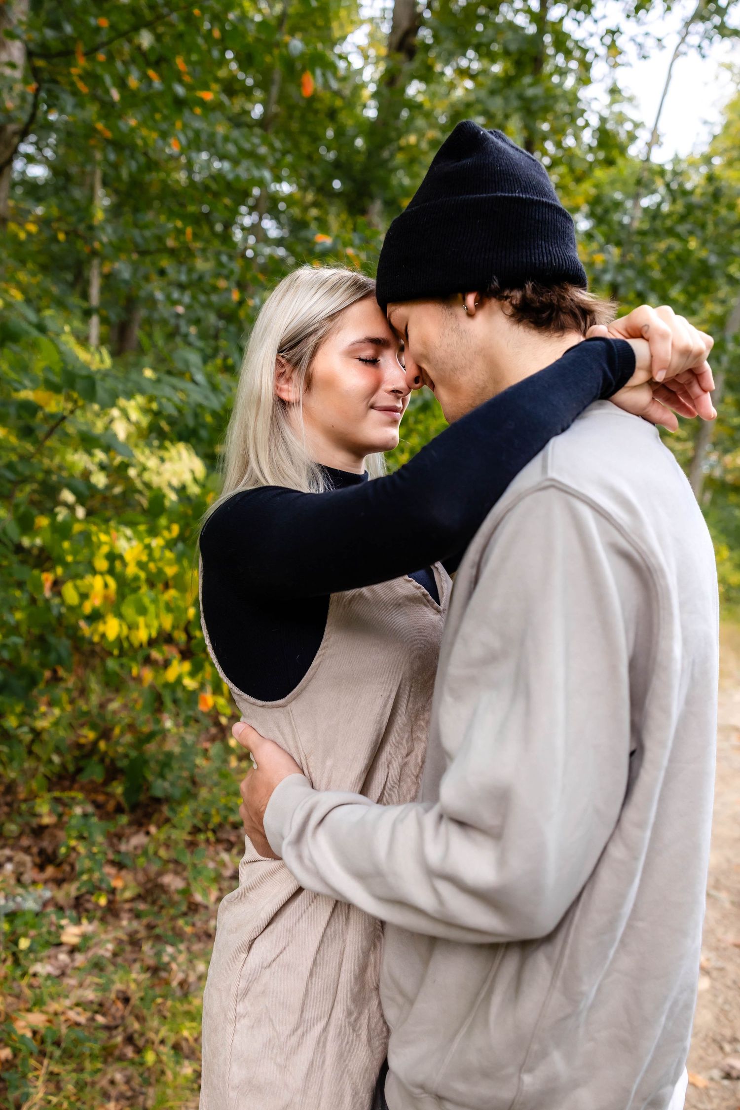 Romantic autumn photoshoot of couple embracing in cozy sweaters against fall foliage background.