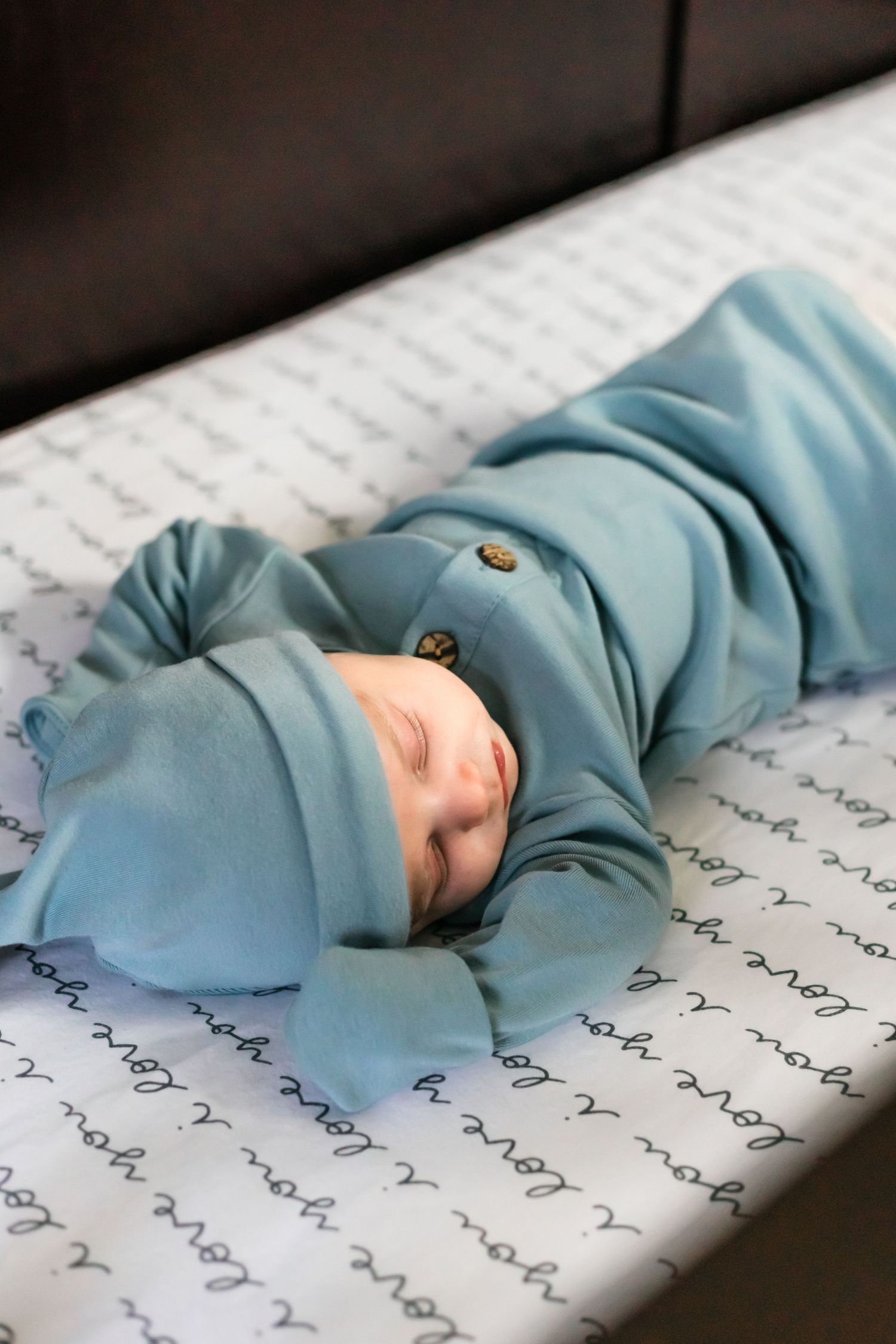 Baby sleeping peacefully on patterned blanket wearing soft blue outfit.