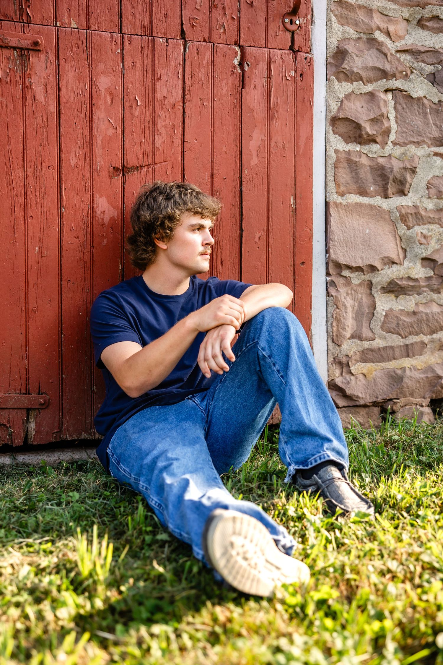 Side profile portrait while sitting against weathered red barn door.