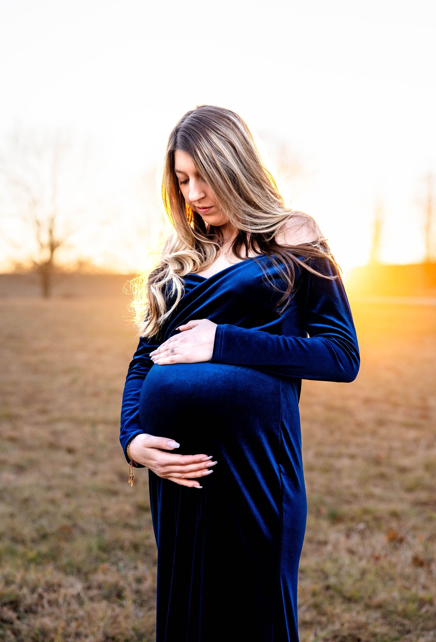 Maternity portrait featuring elegant navy blue velvet dress against golden sunset.