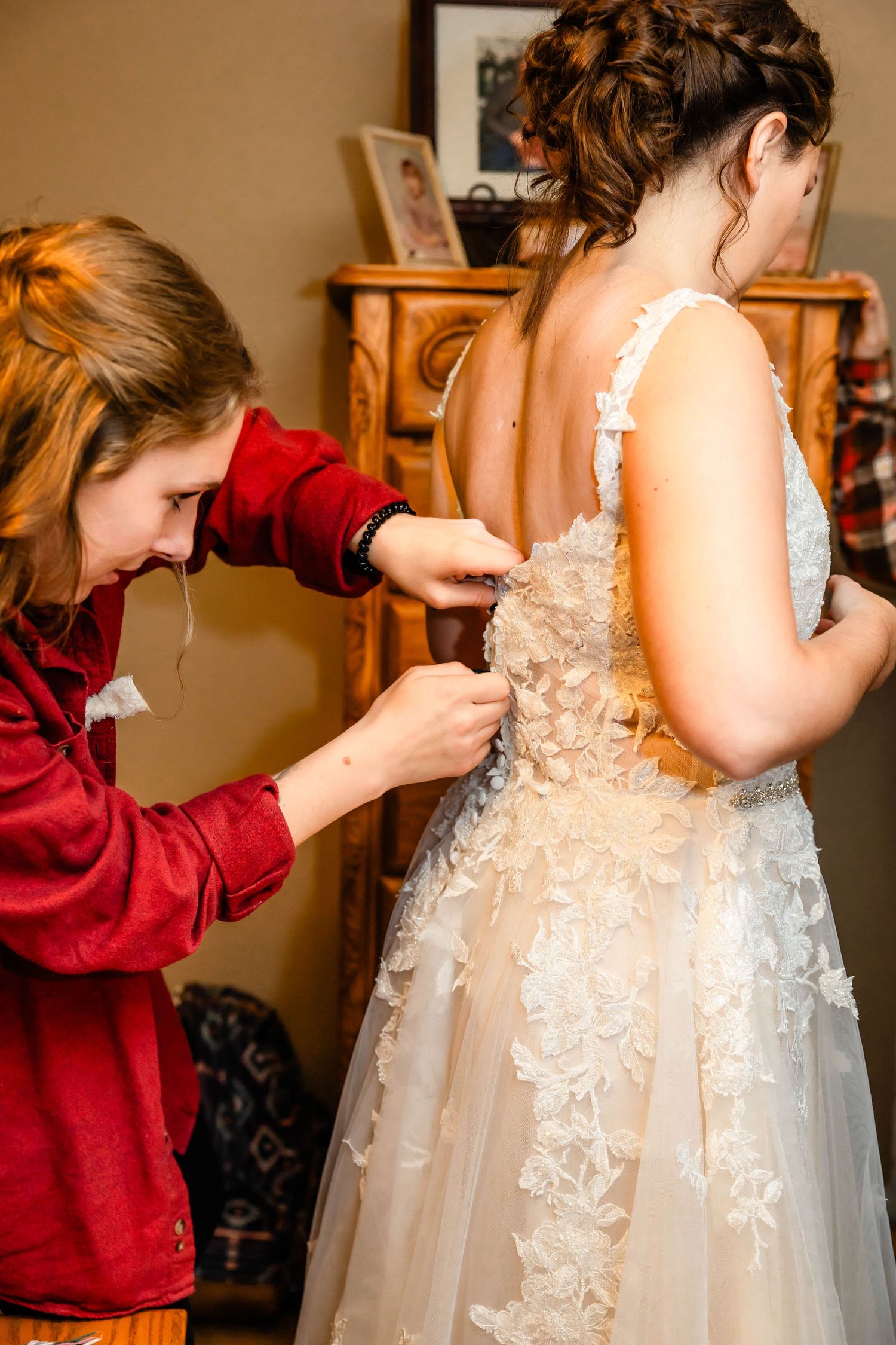 Someone in red assists with buttoning up an intricate lace wedding dress.
