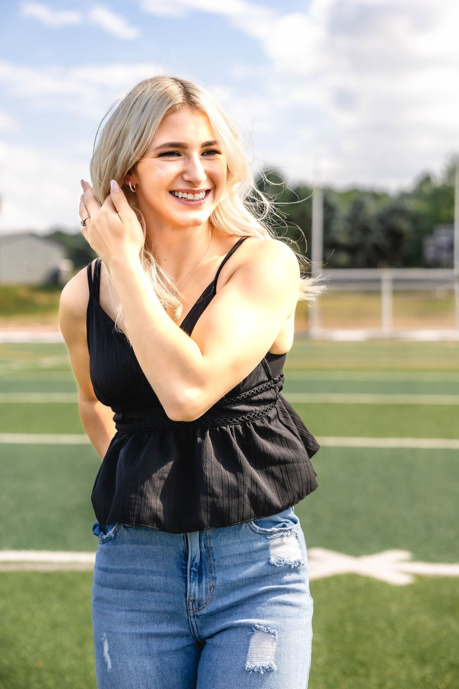 A person in casual summer attire smiles while standing on a football field.