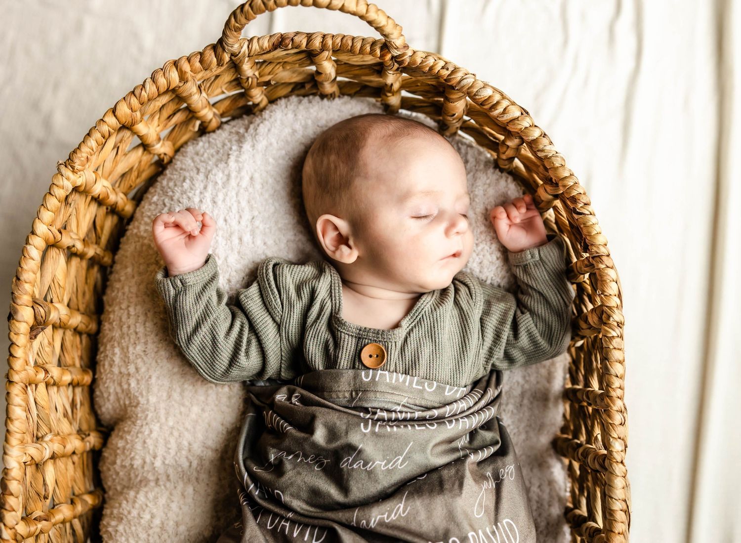 A sleeping infant wearing gray overalls rests peacefully in a woven basket.