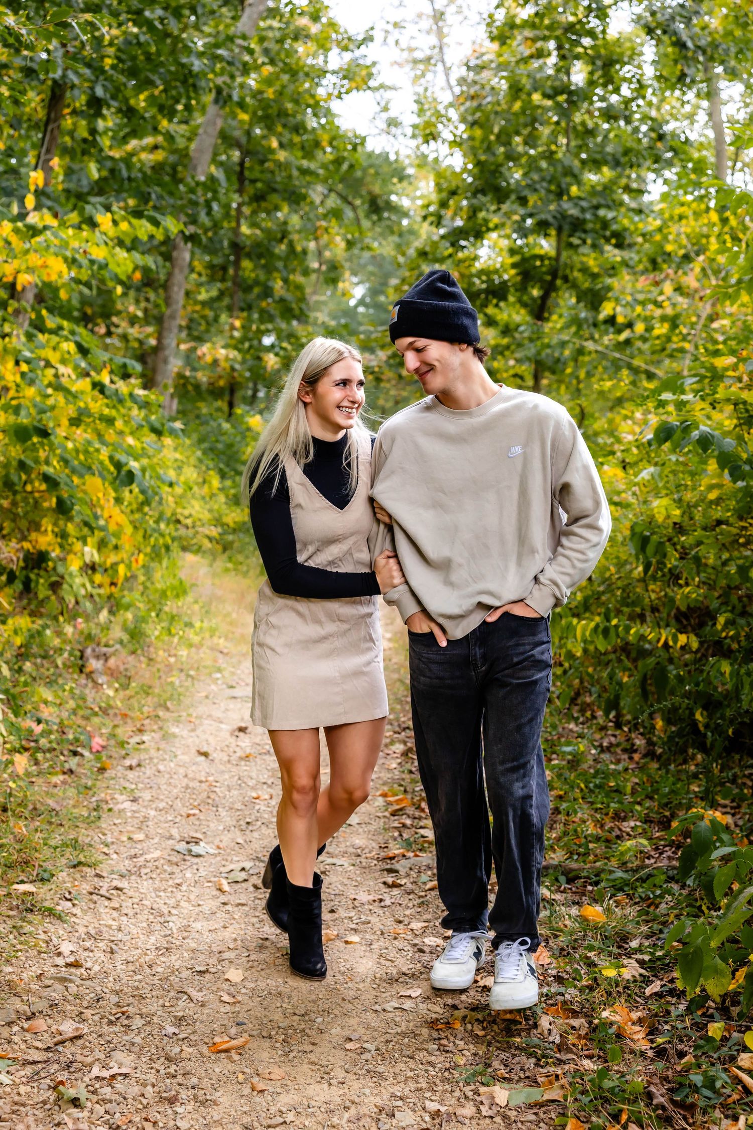 A stylish couple walking together on an autumn trail wearing coordinated casual outfits.