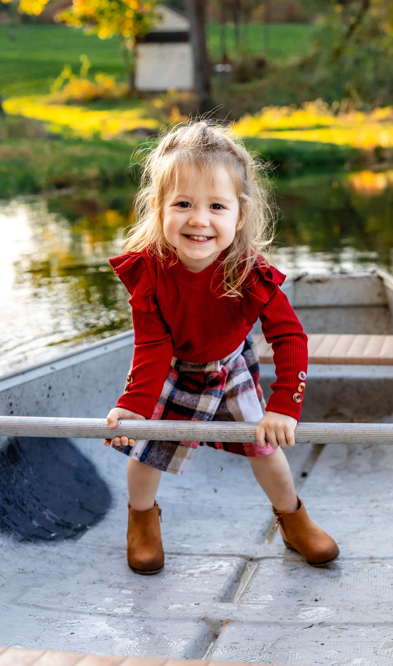 A young child in red sweater and boots plays with canoe oars during fall.