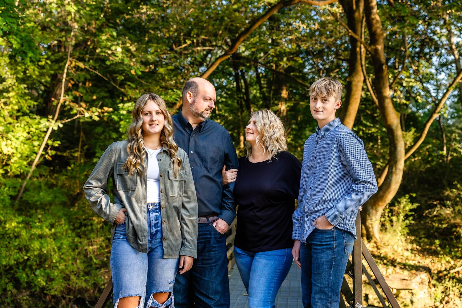 Outdoor family photo with natural sunlight filtering through green trees.