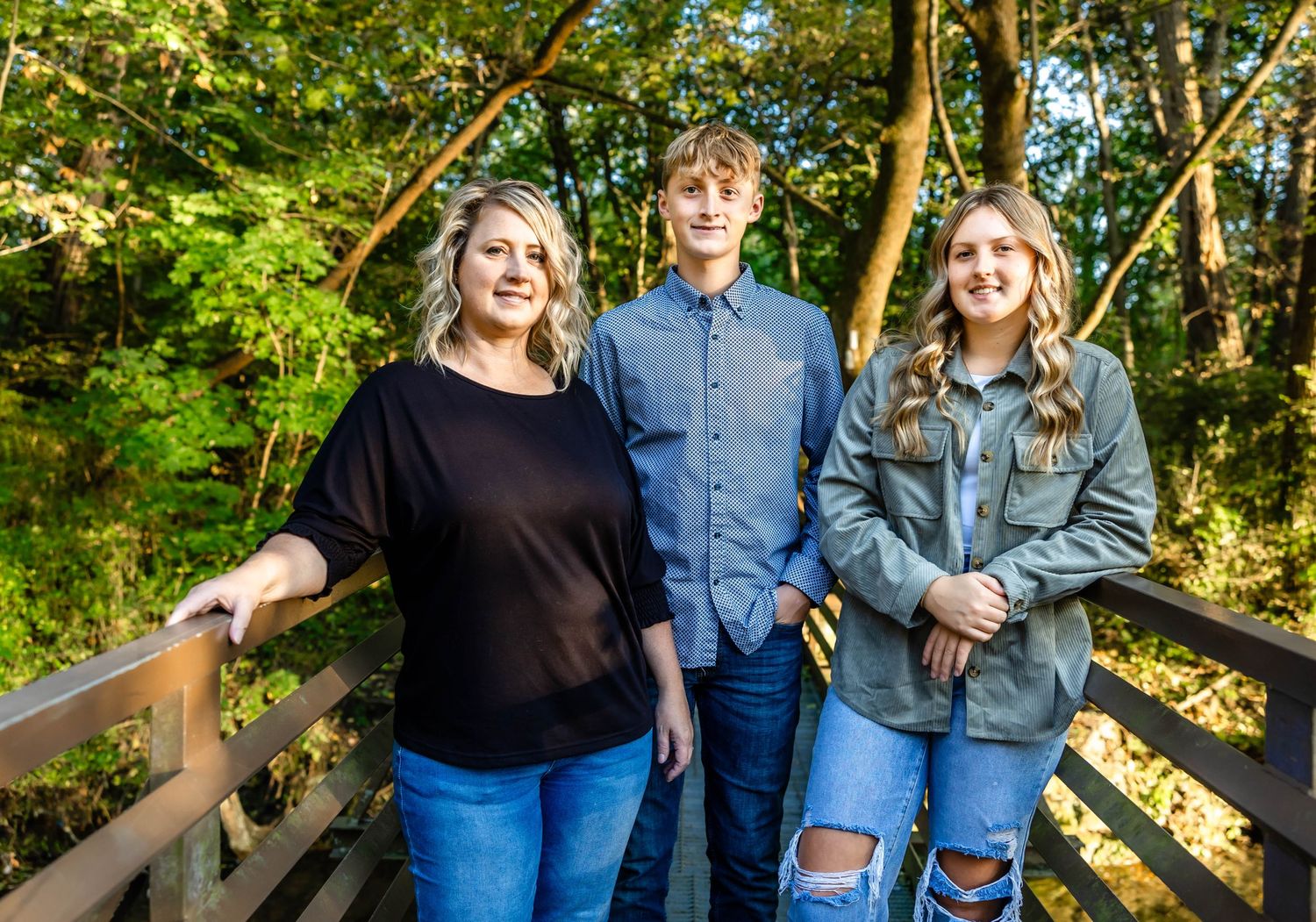 Three people in casual attire standing together on wooden walkway surrounded by green foliage.