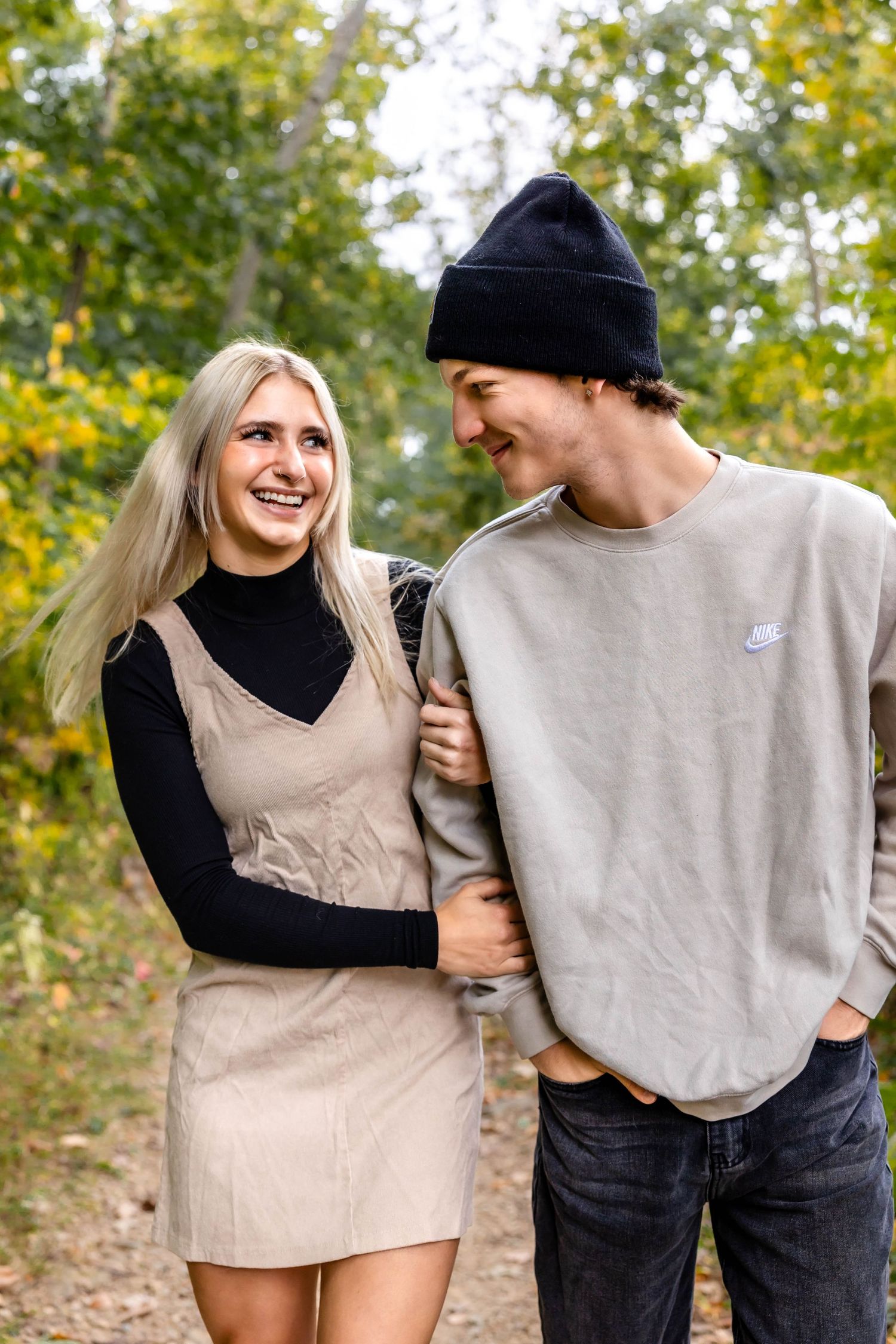A couple laughing together on an autumn trail wearing coordinated beige and black outfits.