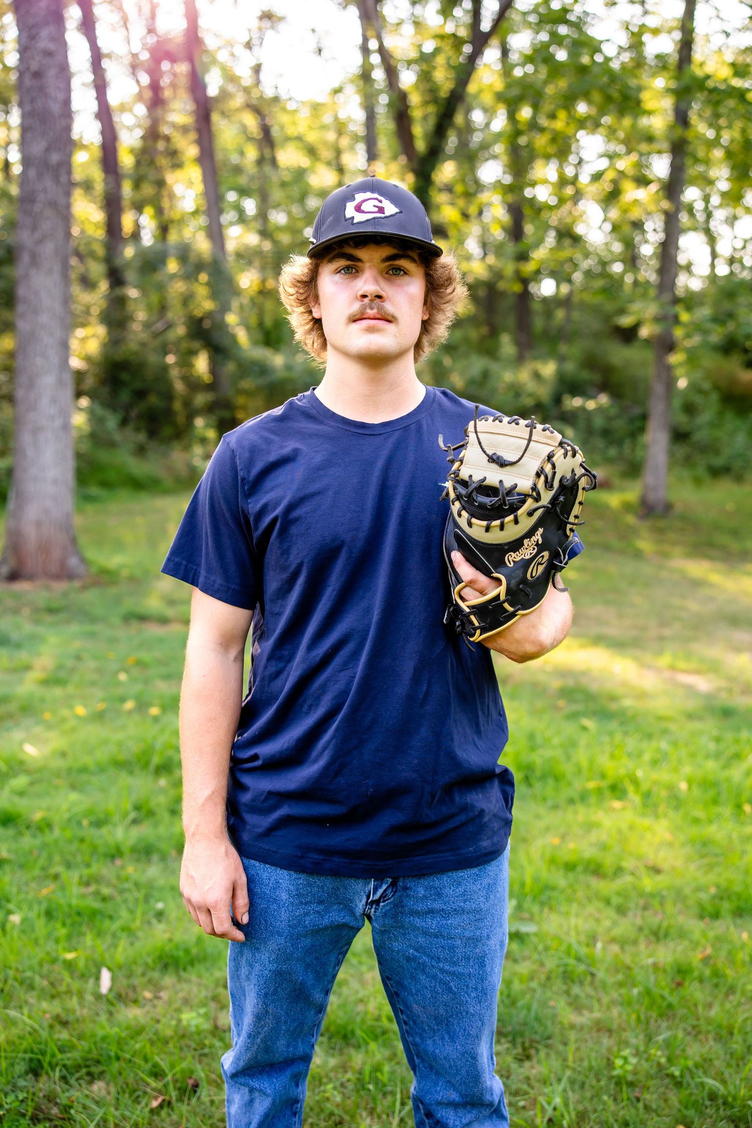 Person wearing baseball cap and navy shirt displays leather baseball glove in outdoor setting.