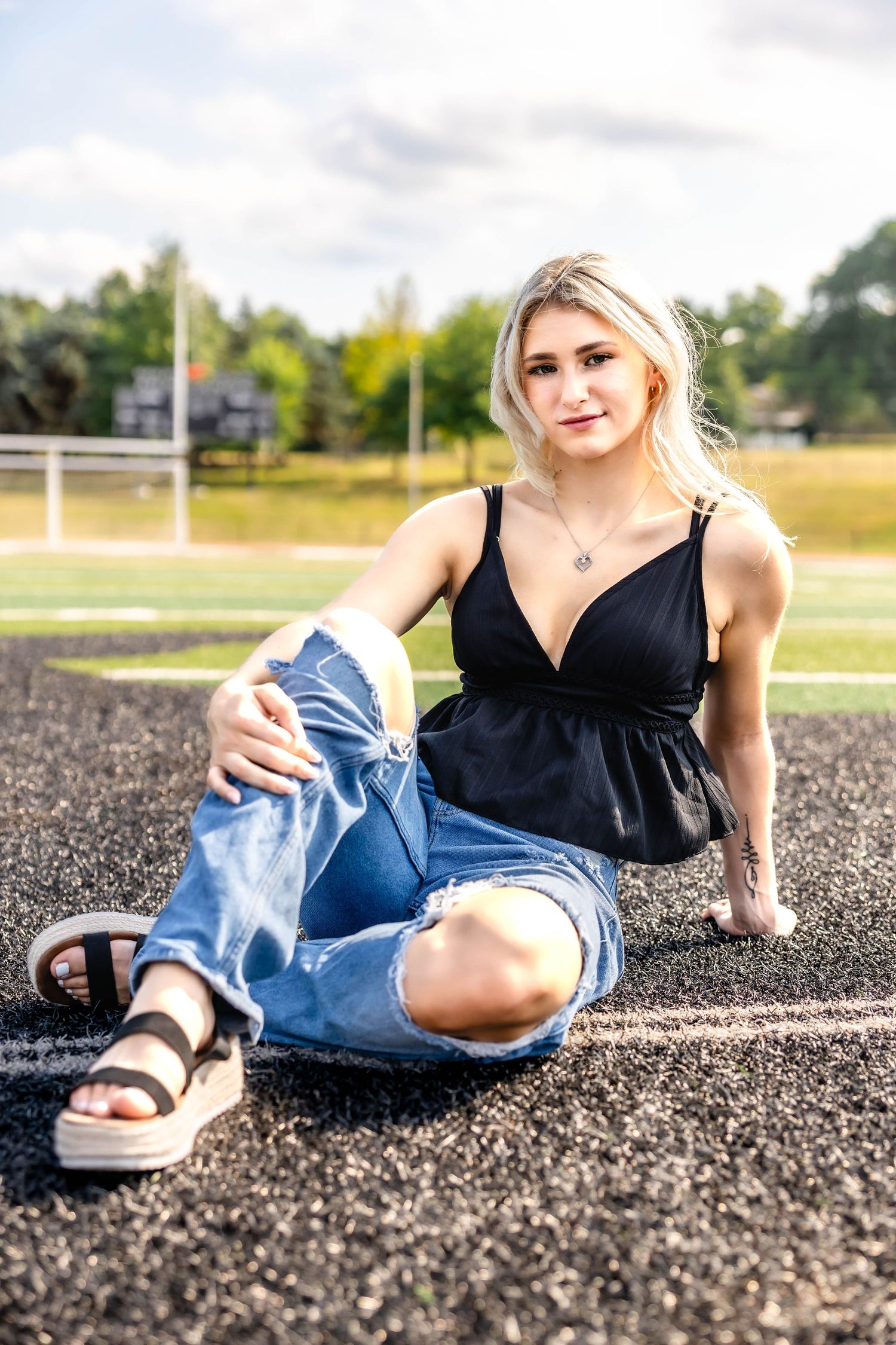 Casual outdoor photoshoot on a track wearing ripped jeans and sandals.