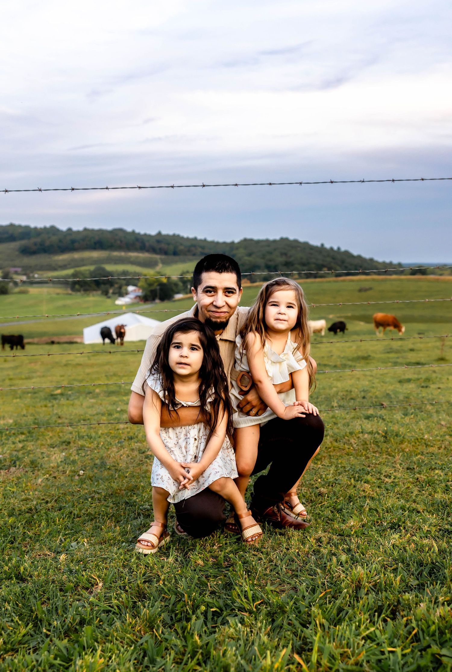 A group poses together on a grassy hillside with farm animals visible in the background.