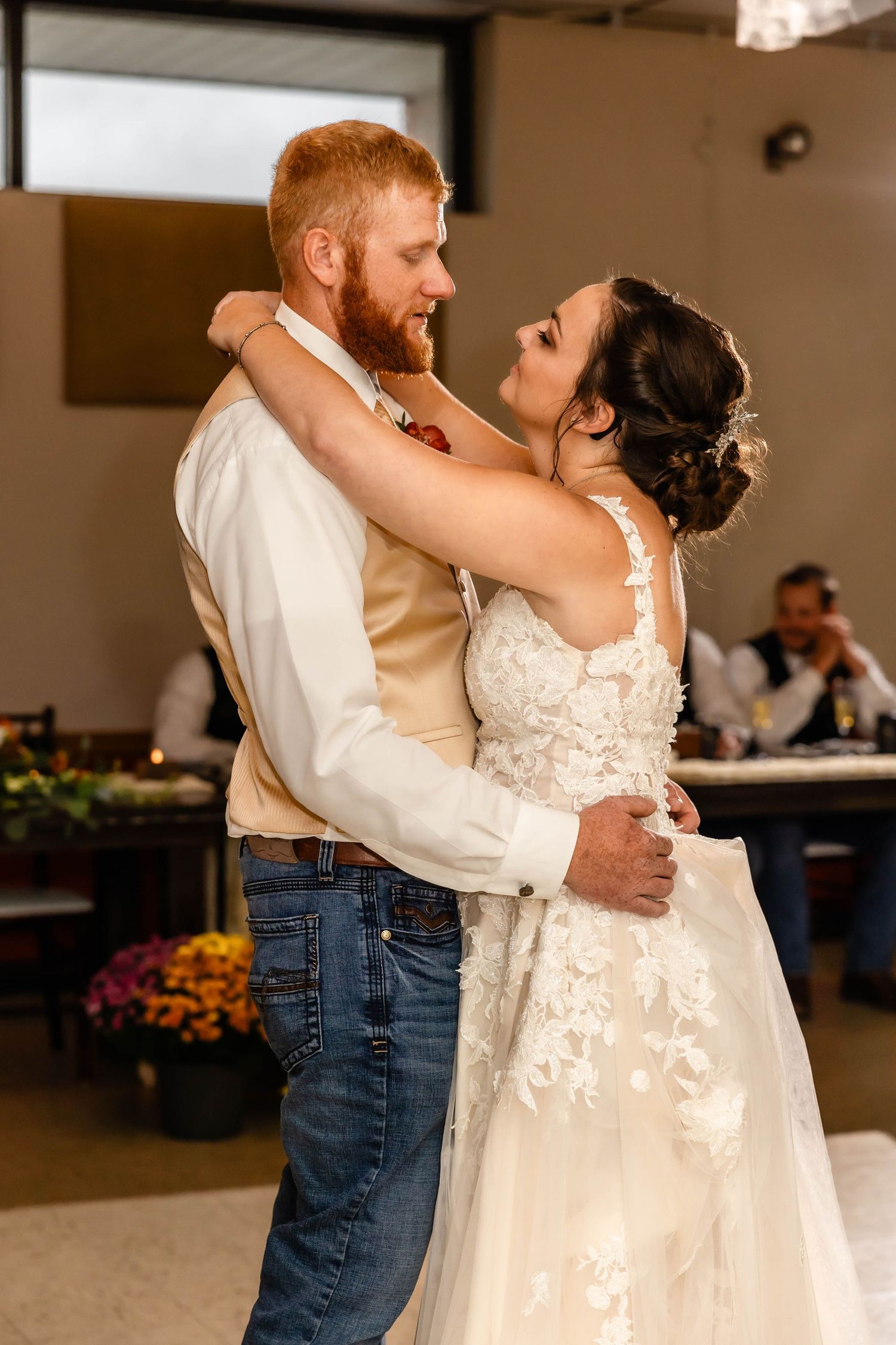 A tender embrace shared during a wedding dance in a reception hall with autumn decorations.
