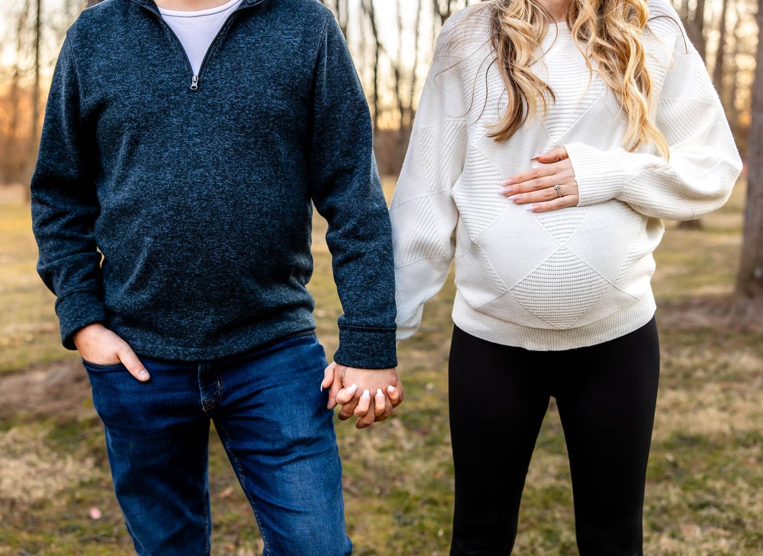 Close-up shot showing expectant couple holding hands, wearing coordinating navy and white sweaters.