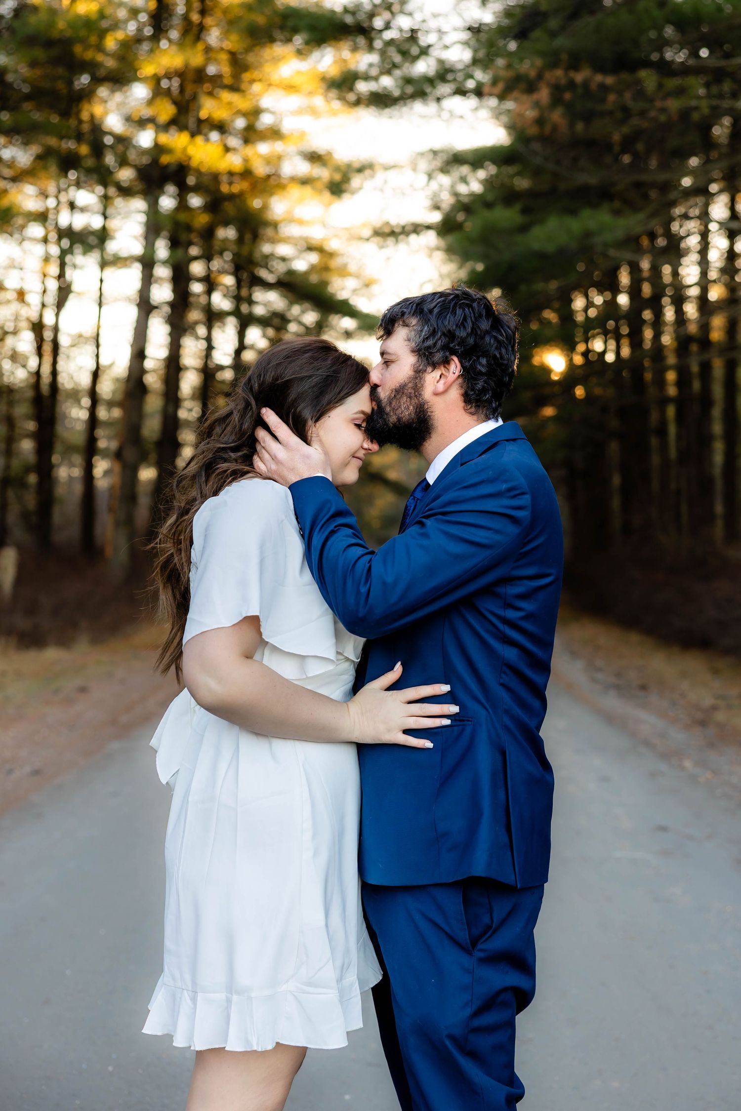 A romantic sunset moment between a couple in formal attire on a forest path.