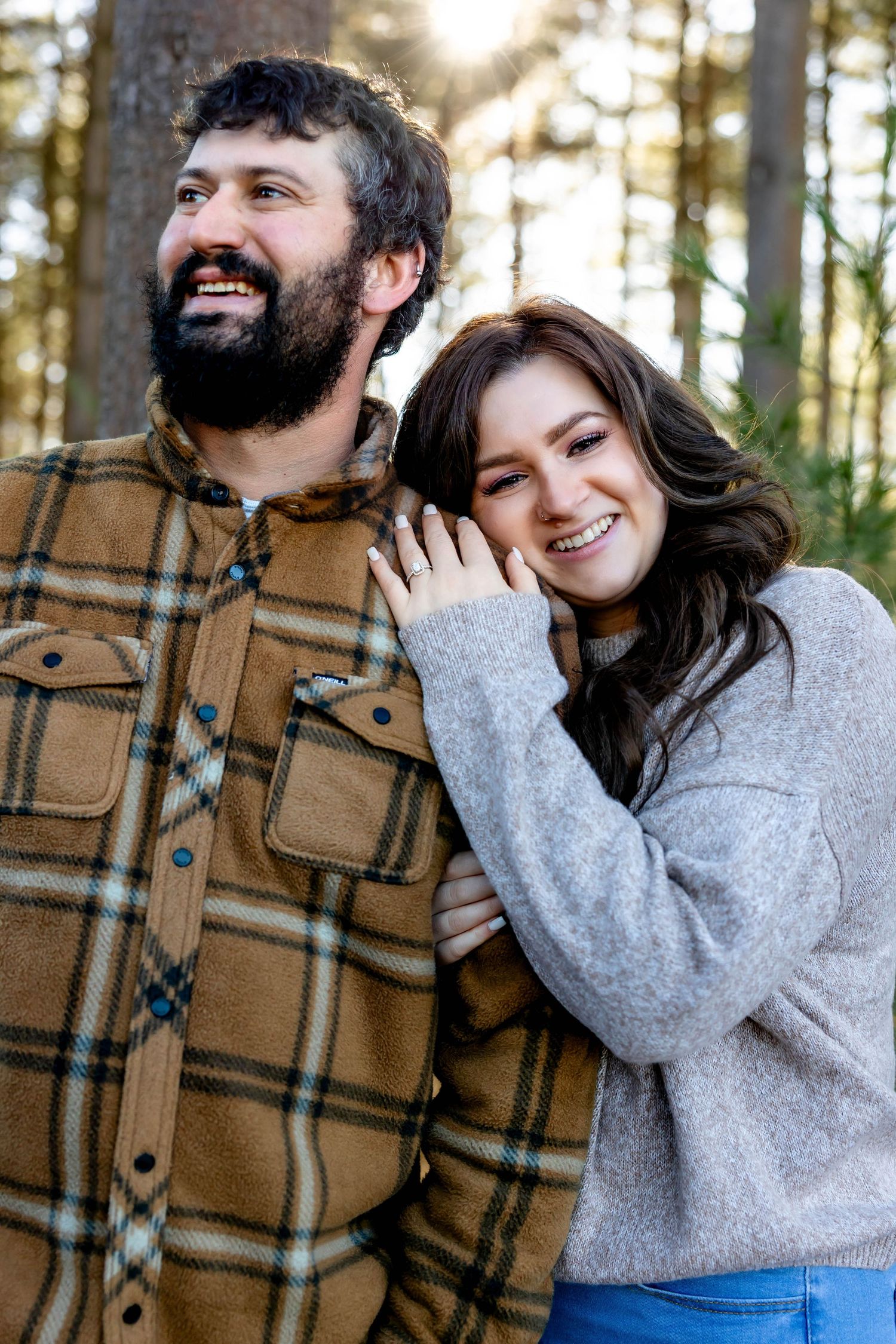 Happy couple laughing together in sunlit forest wearing casual clothing.