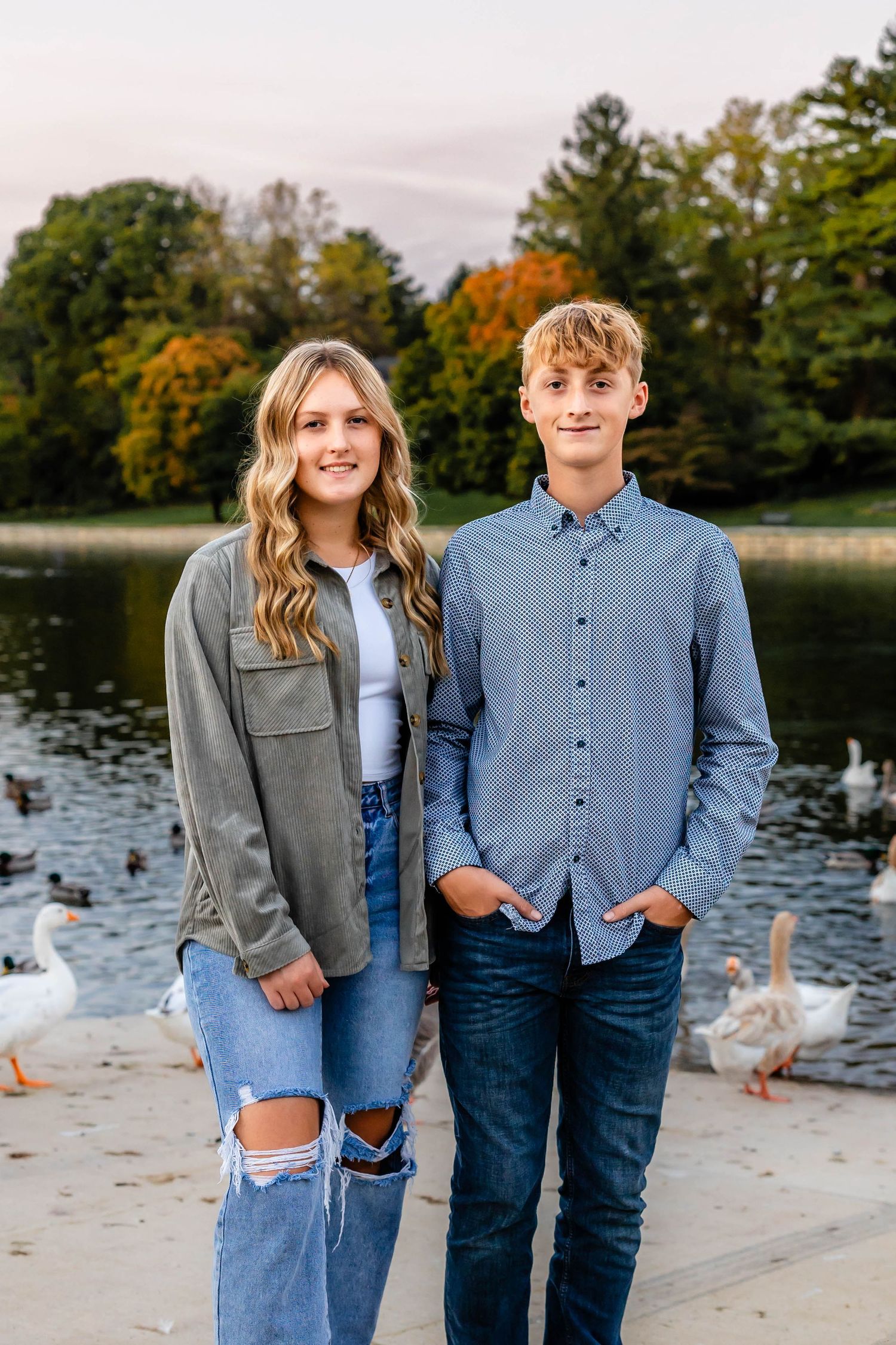 Young couple in casual attire poses by a lake during autumn.