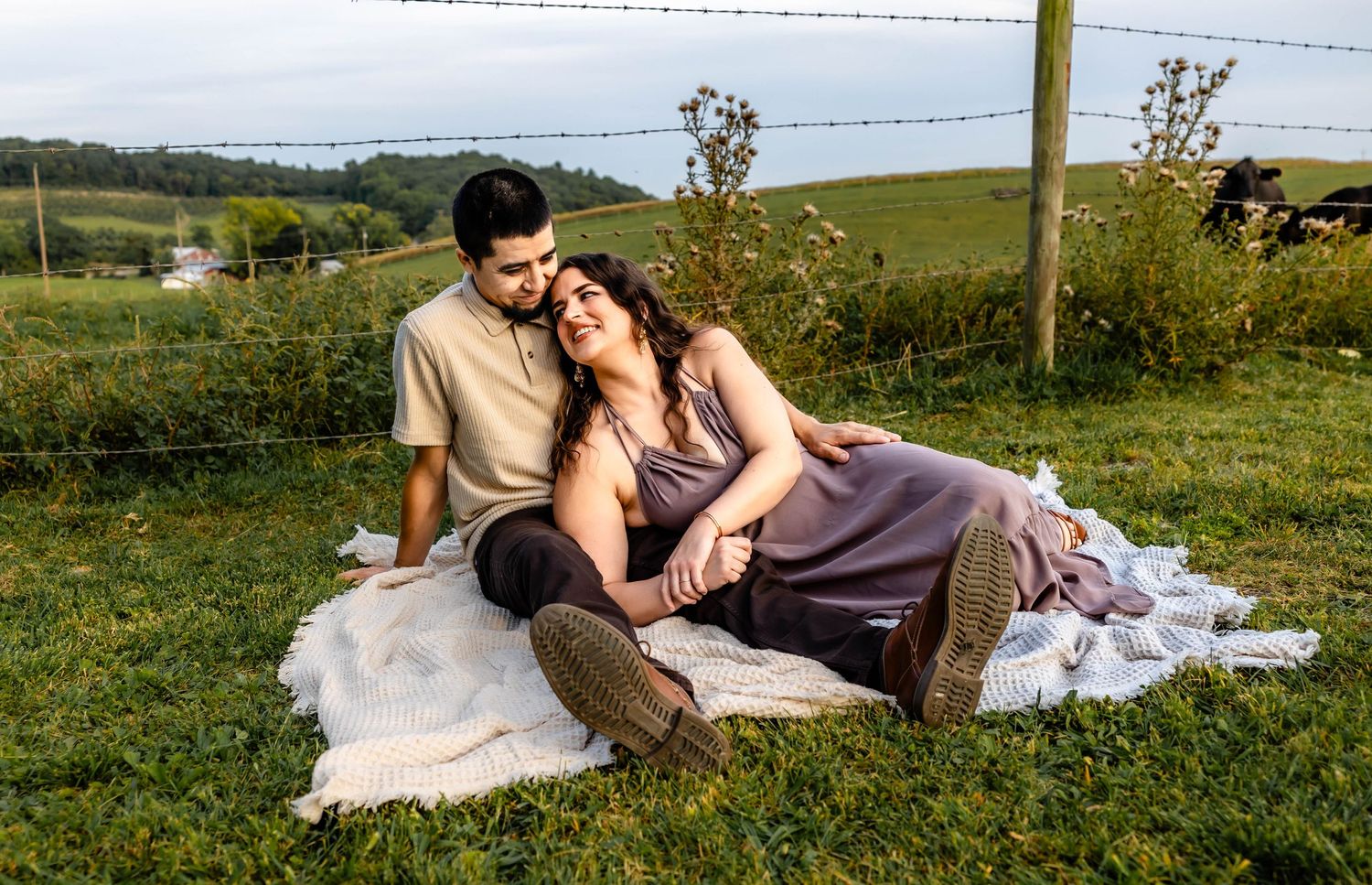 Two people sharing an intimate moment while lounging on a white blanket in a grassy field.