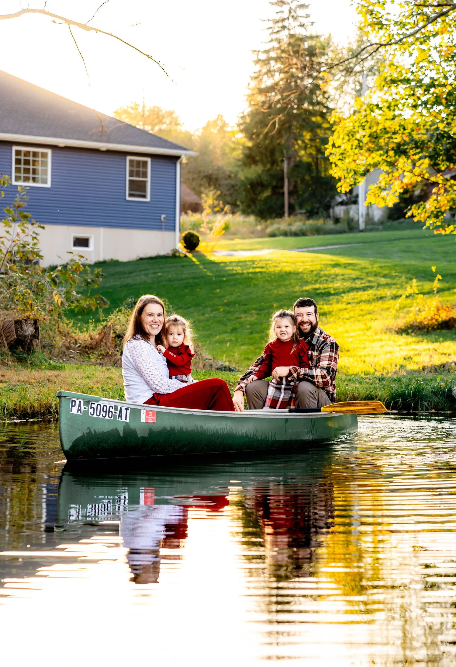 Family enjoys autumn afternoon in green canoe on pond near blue house.