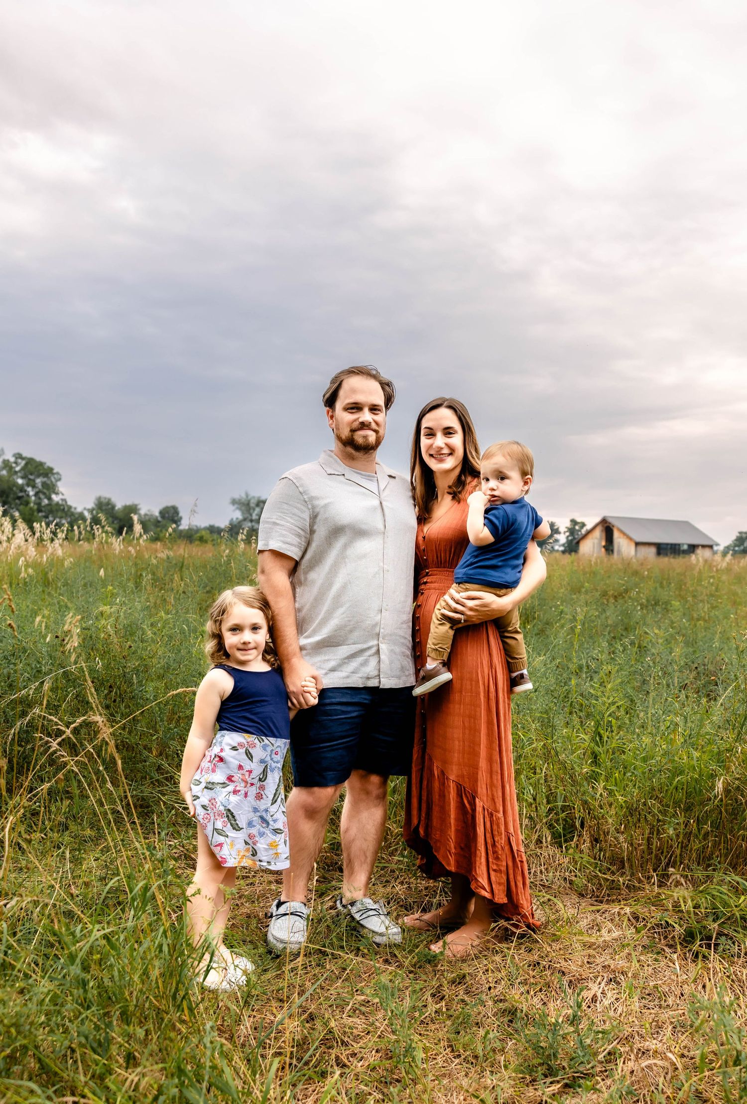 Summer family portrait in tall grass field with houses in background.