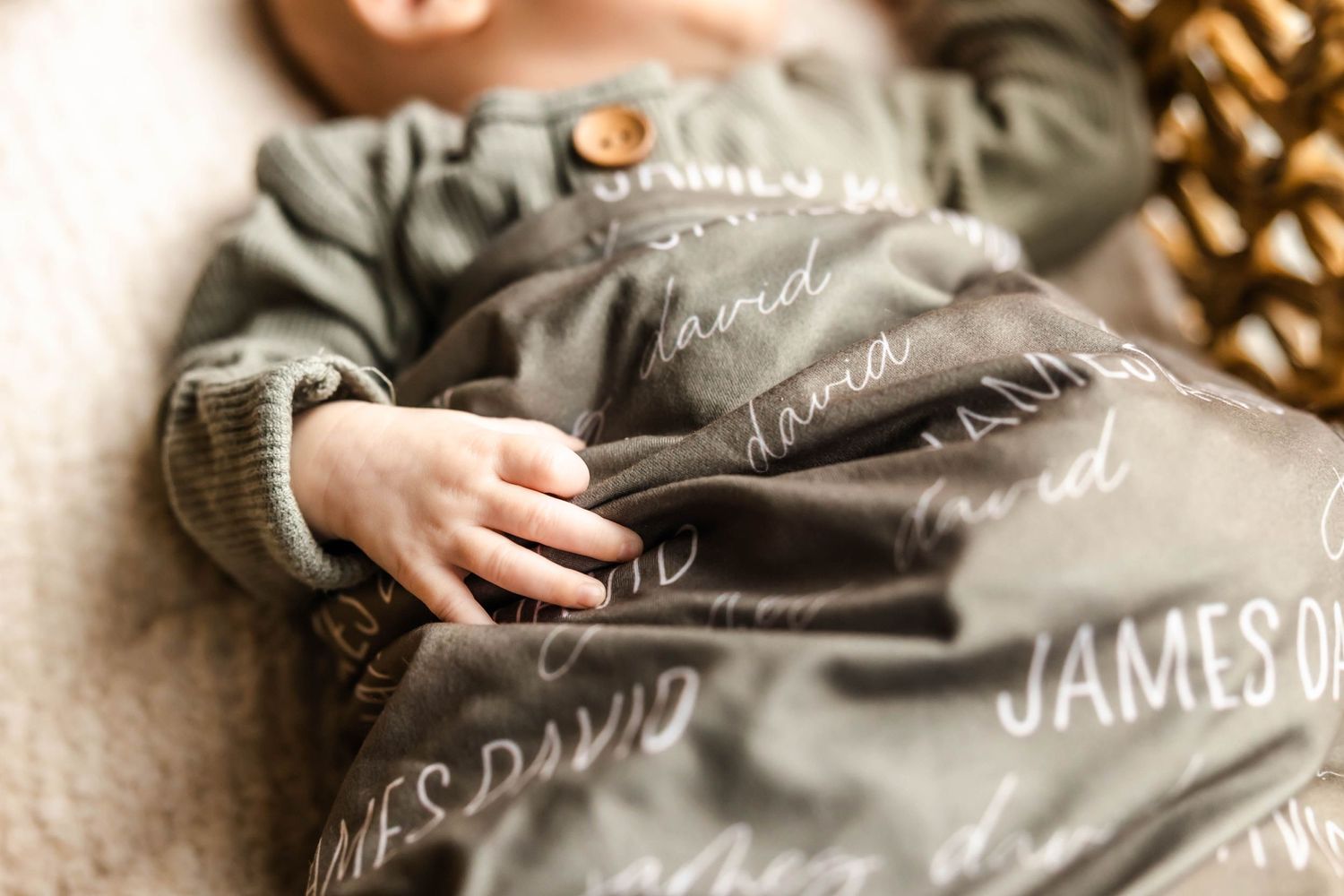 Close-up detail of tiny hand on personalized gray baby swaddle with text.