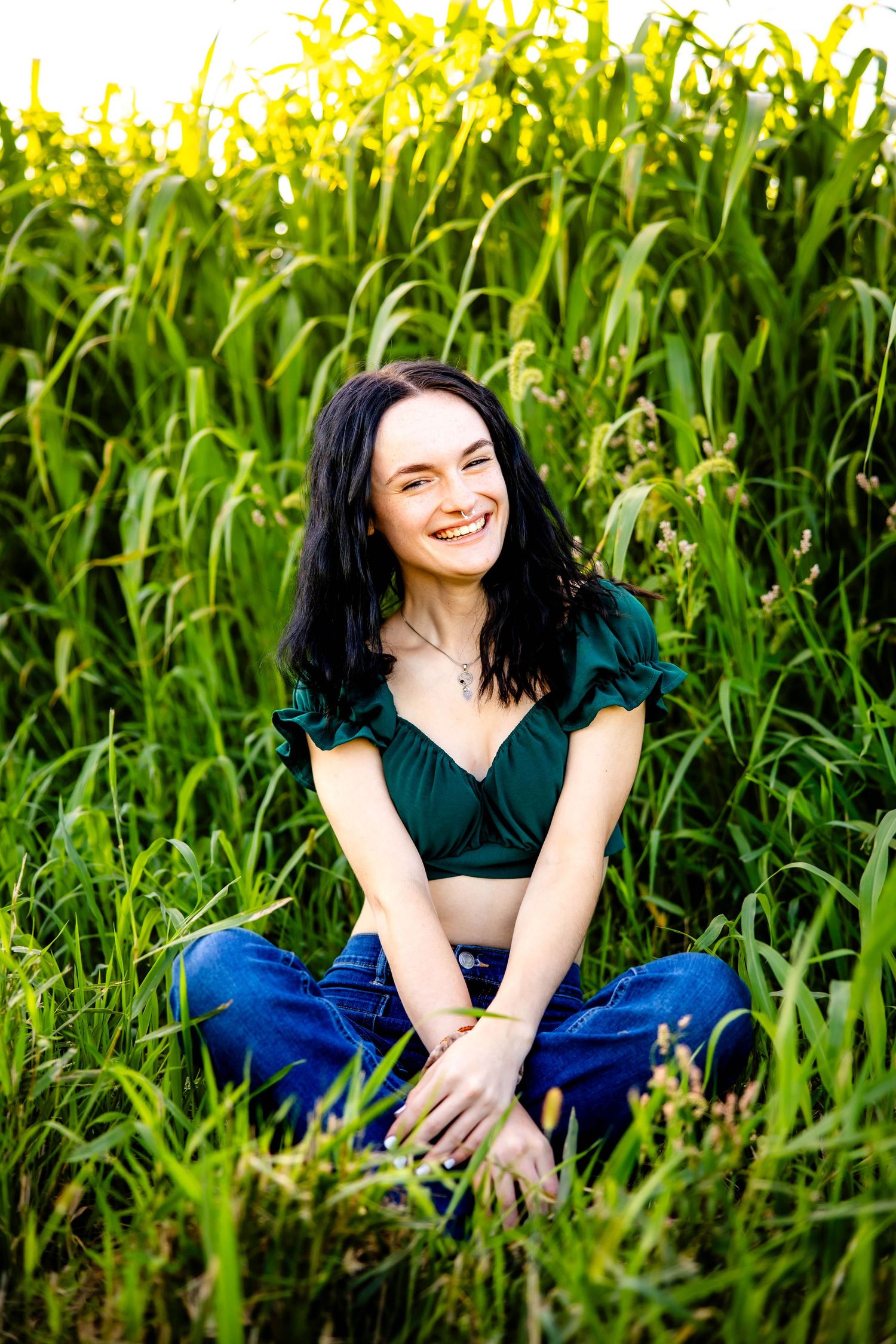 A person wearing emerald green sits in tall grass with a bright cornfield backdrop.
